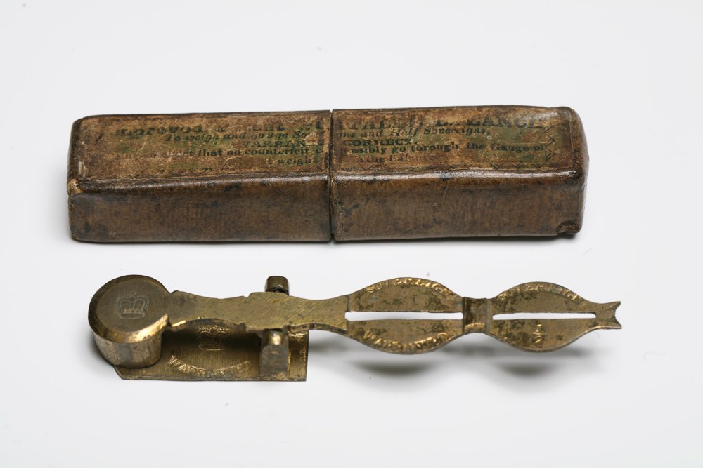 Half Sovereign Balance in Original Box: An antique half sovereign coin scale; the counterweight has the image of a crown inscribed on top and on the base, with SOVEREIGN above and WARRANTED below. The original box is inscribed IMPROVED PATE