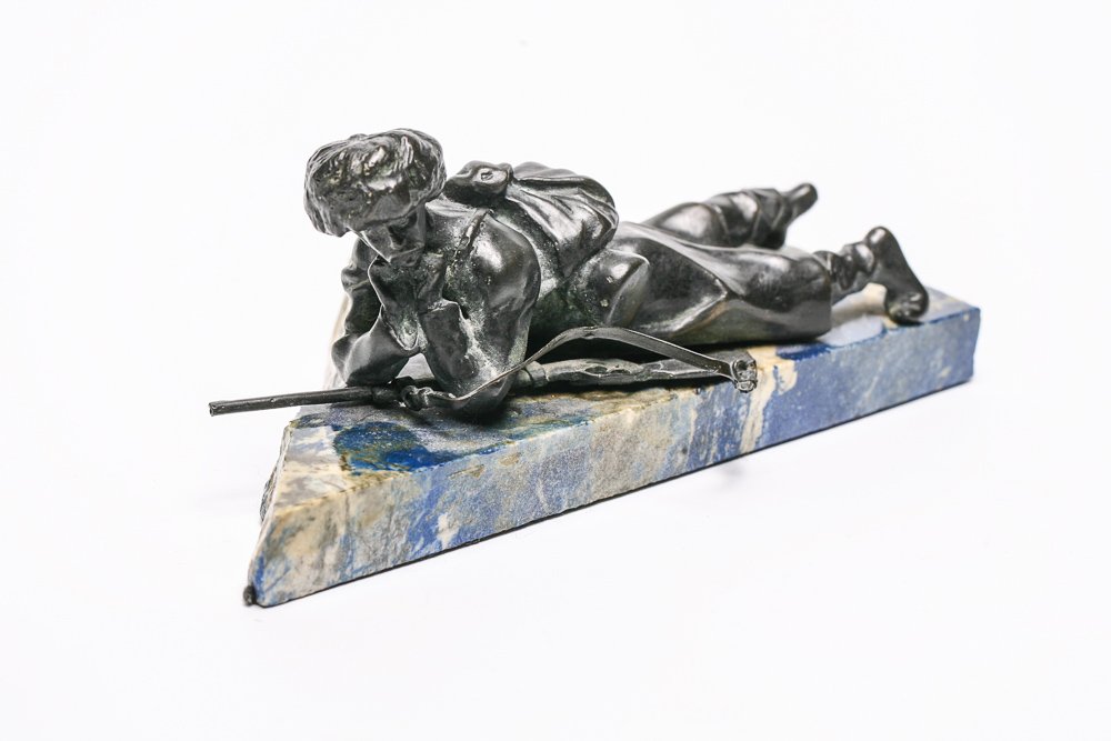 Russian Bronze Solder Statue: An early 20th century Russian bronze of a soldier lying prone with a rifle. He is wearing a Papakha hat and a great coat as was typical before the great war. Mounted to jagged marble plinth. Unsigned.
