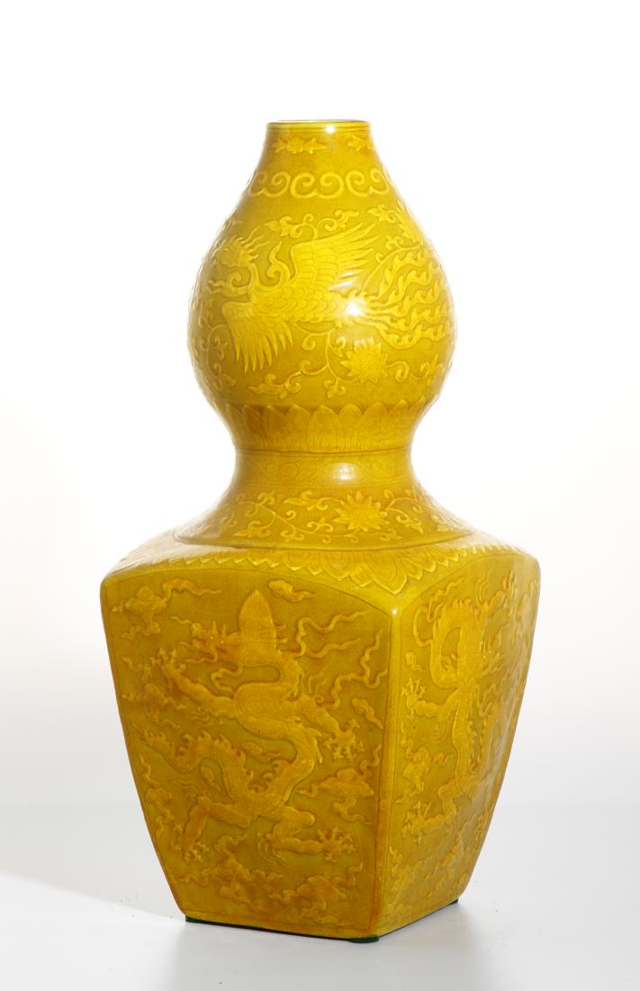 Yellow Enameled Double-Gourd Vase: Comprising a square lower section surmounted with a globular upper section, each of the square panels carved in relief with a writhing dragon amidst ruyi clouds, the upper globular section carved in
