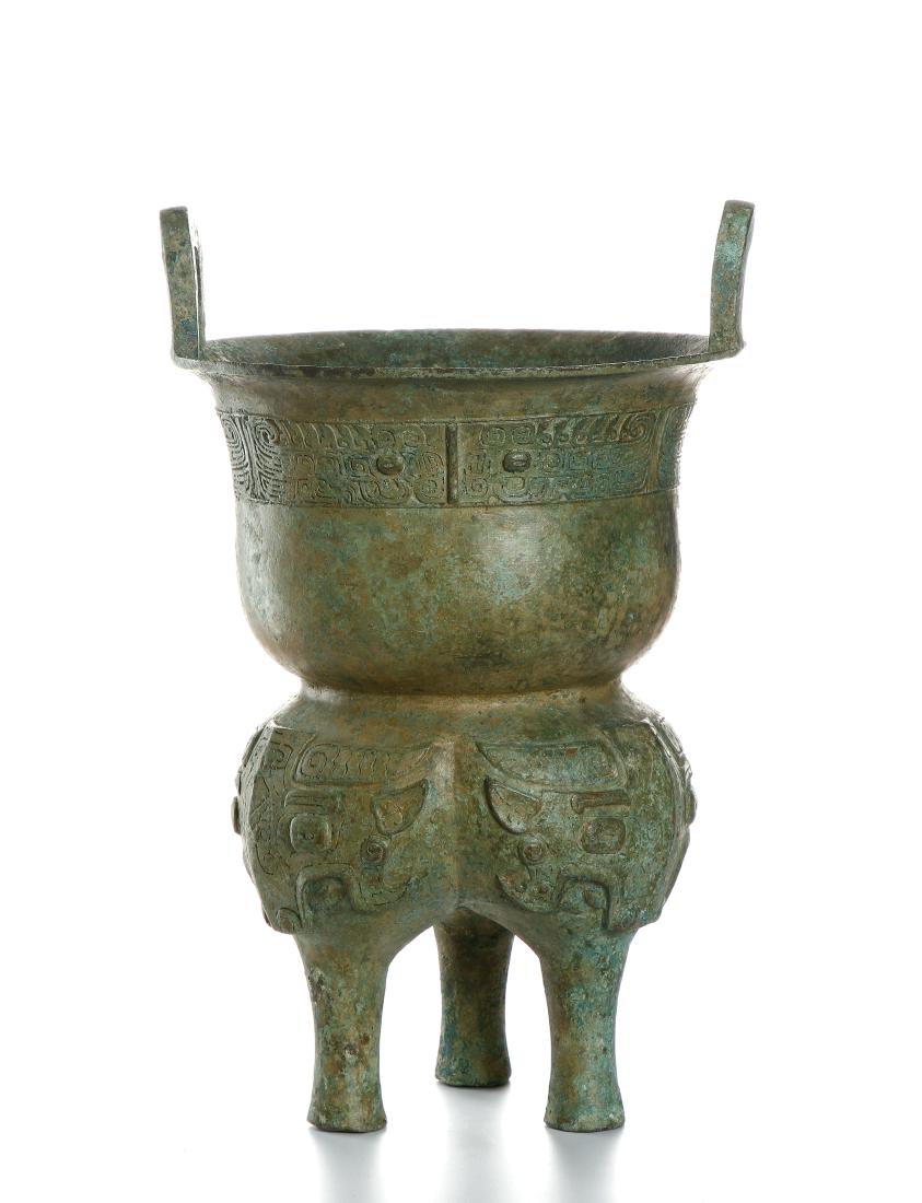 Chinese Archaic Bronze Bronze Vessel: cast to resemble an archaic steamer, the lower section divided into three bulbous lobes tapering to three columnar feet, each lobe cast with a taotie mask, , below triangular flanges on the sides of t