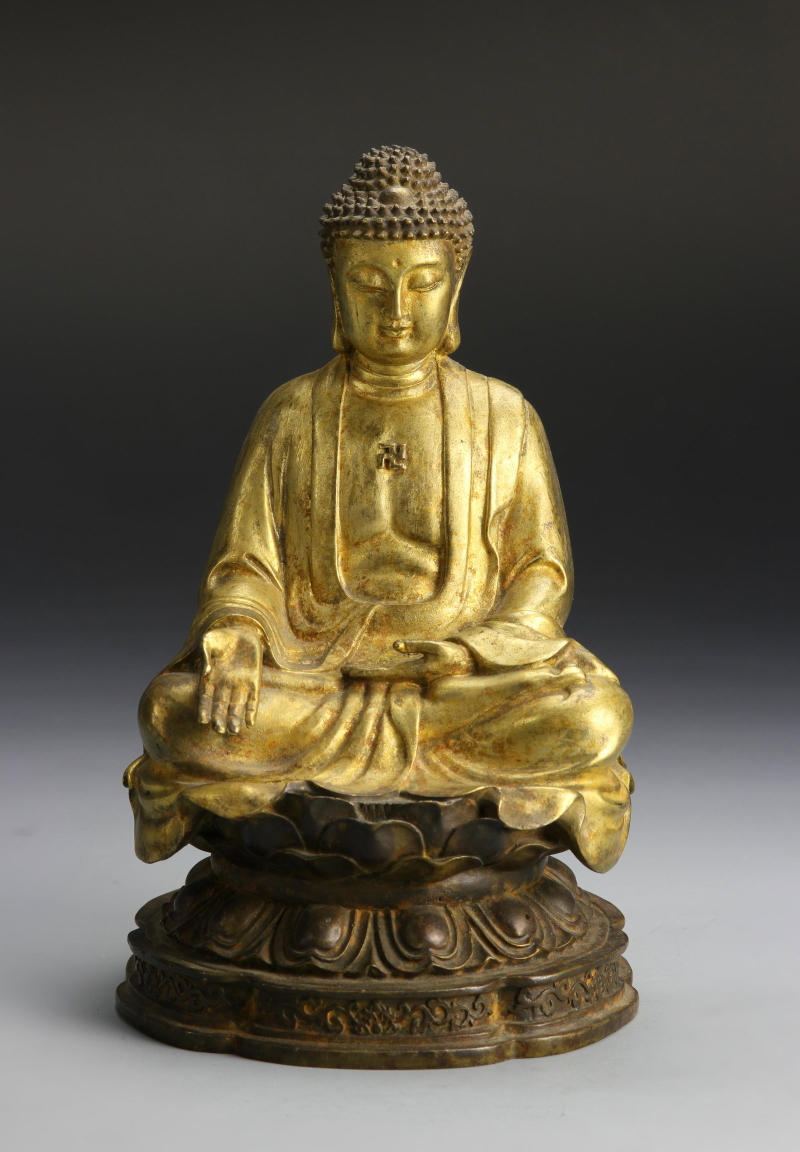 Chinese Gilt-Bronze Figure of Shakyamuni Buddha: In a seated position, on a lotus flower, with outstretched hand, and flowing robes. Height 7 1/2 in.