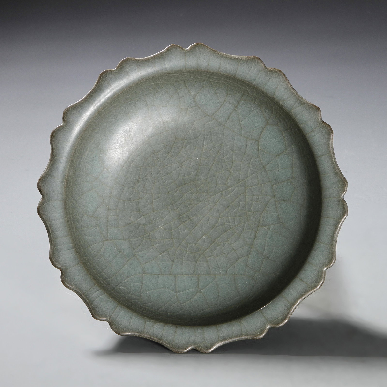 Longquan Kuan-Type Foliate-Rim Dish: The shallow rounded sides rising from a short tapered foot to an everted foliate rim, covered overall in a mottled bluish-green glaze suffused with russet crackles, base with six spur marks, 7 in wide