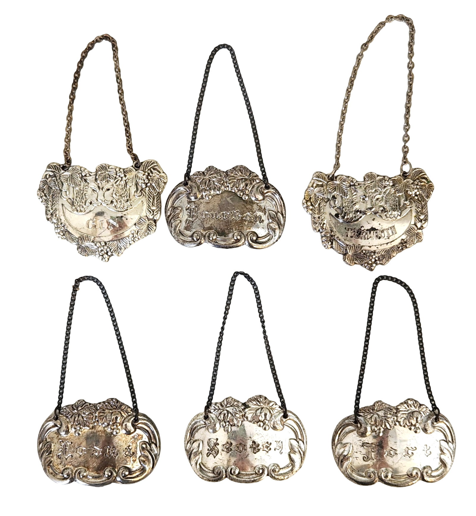 Set of Six Antique Liquor Decanter Labels: A fine collection of six antique decanter labels, each ornately decorated with repoussé floral and vine motifs. The labels are inscribed with popular liquor names: Gin, Brandy, Vermouth, Bourbon, Sco