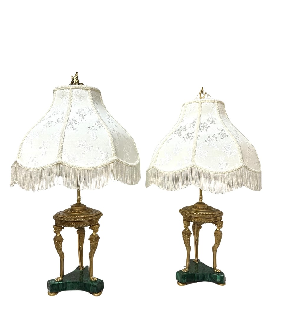 Pair of Bronze and Malachite Neoclassical Table Lamps with Fringe Shades: Exquisite pair of neoclassical table lamps featuring finely cast gilt bronze tripodal bases with figural supports—each leg depicting a classical male bust with curled hair and draped detail, termina