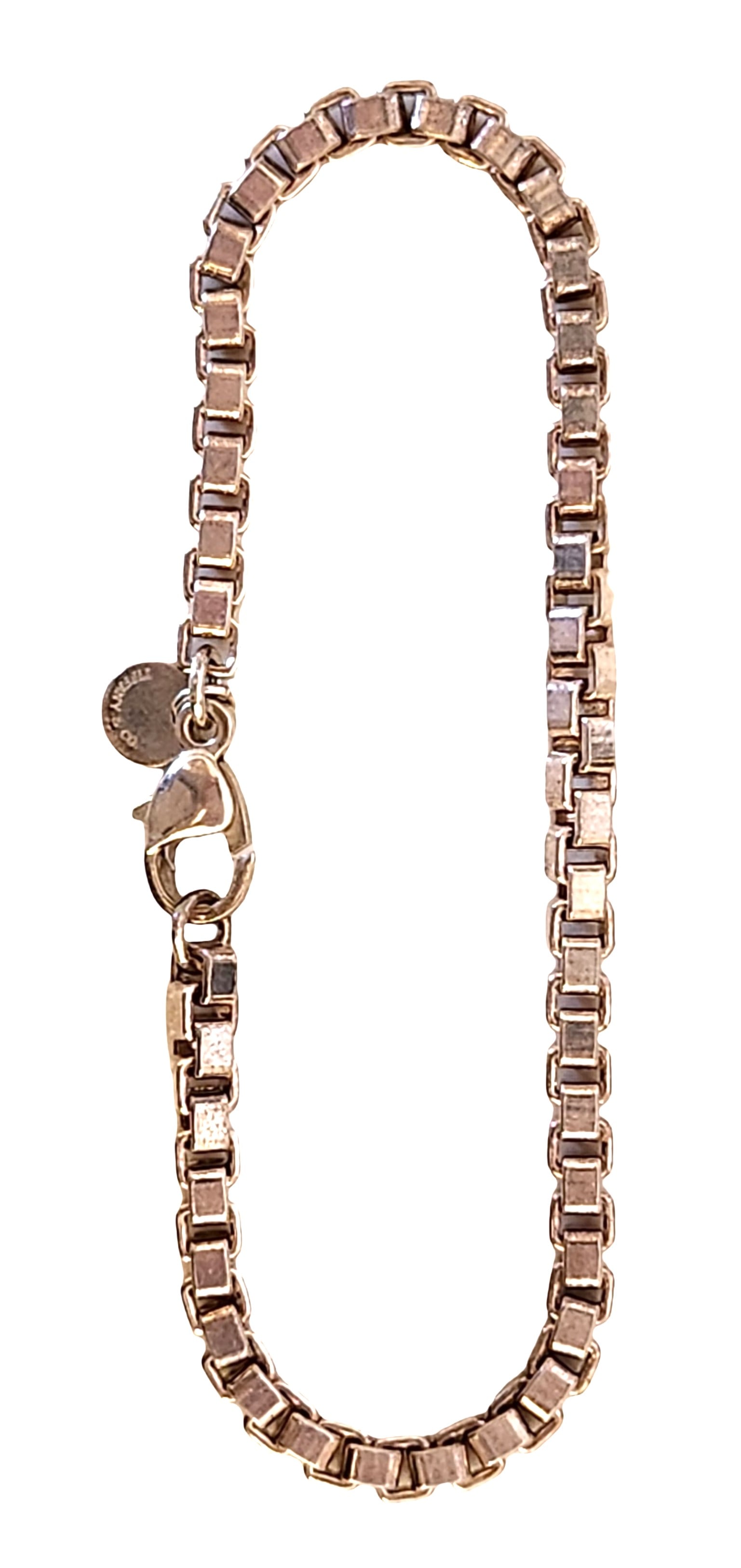 Tiffany & Co. Sterling Silver Box-Link Bracelet: A classic Tiffany & Co. sterling silver box-link bracelet, crafted with the iconic square-link chain and finished with a sturdy lobster clasp. A small round charm near the clasp is stamped “TIFFANY