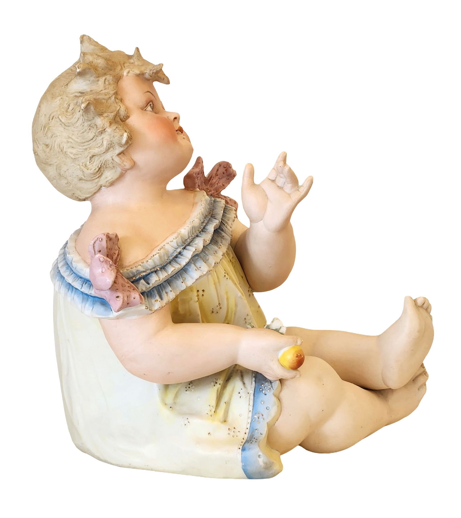 Large German Bisque Porcelain Figure of a Child with Fruits: Charming large German bisque porcelain figure depicting a seated child holding fruits, wearing a pastel yellow dress with blue trim and pink bows. The delicate modeling captures lifelike details and a