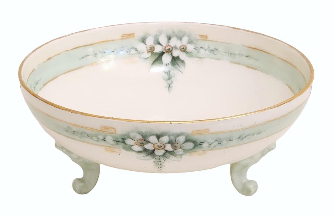 Limoges Porcelain Footed Bowl with Floral Decoration, France: French porcelain footed bowl produced in Limoges, featuring a softly scalloped oval form raised on three molded feet. The bowl is decorated with delicate white floral sprays set against a pale green b