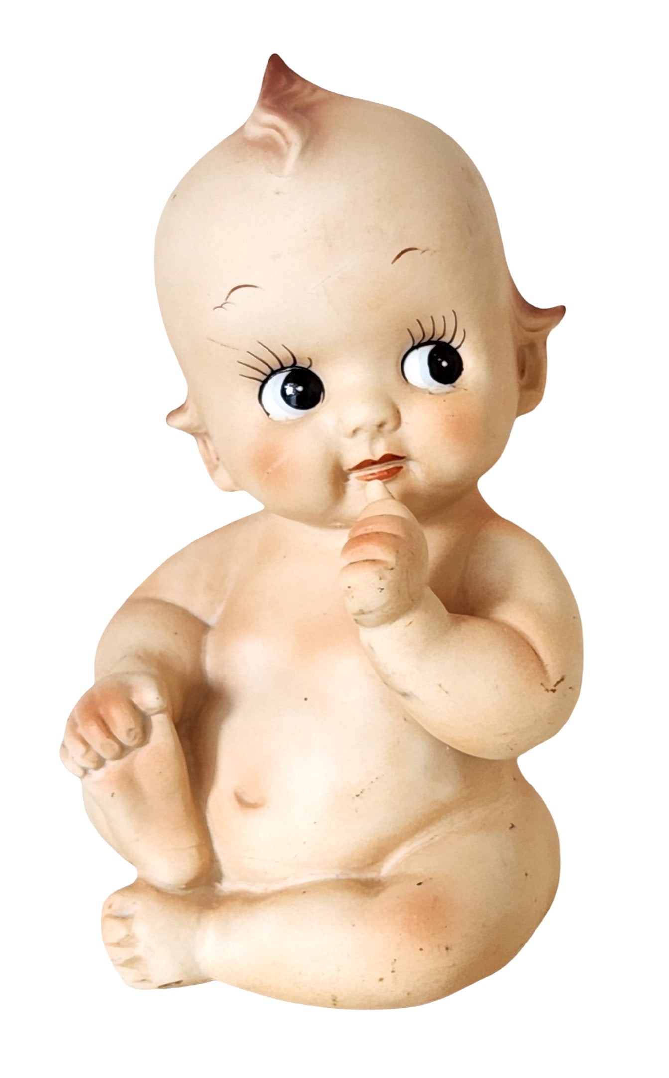 Vintage Ceramic Baby Figurine with Coin Slot, Mid-20th Century: Vintage ceramic baby figurine modeled in a seated pose with one finger raised to the mouth, featuring expressive painted eyes, blushed cheeks, and softly modeled hair details. The figure is finished i