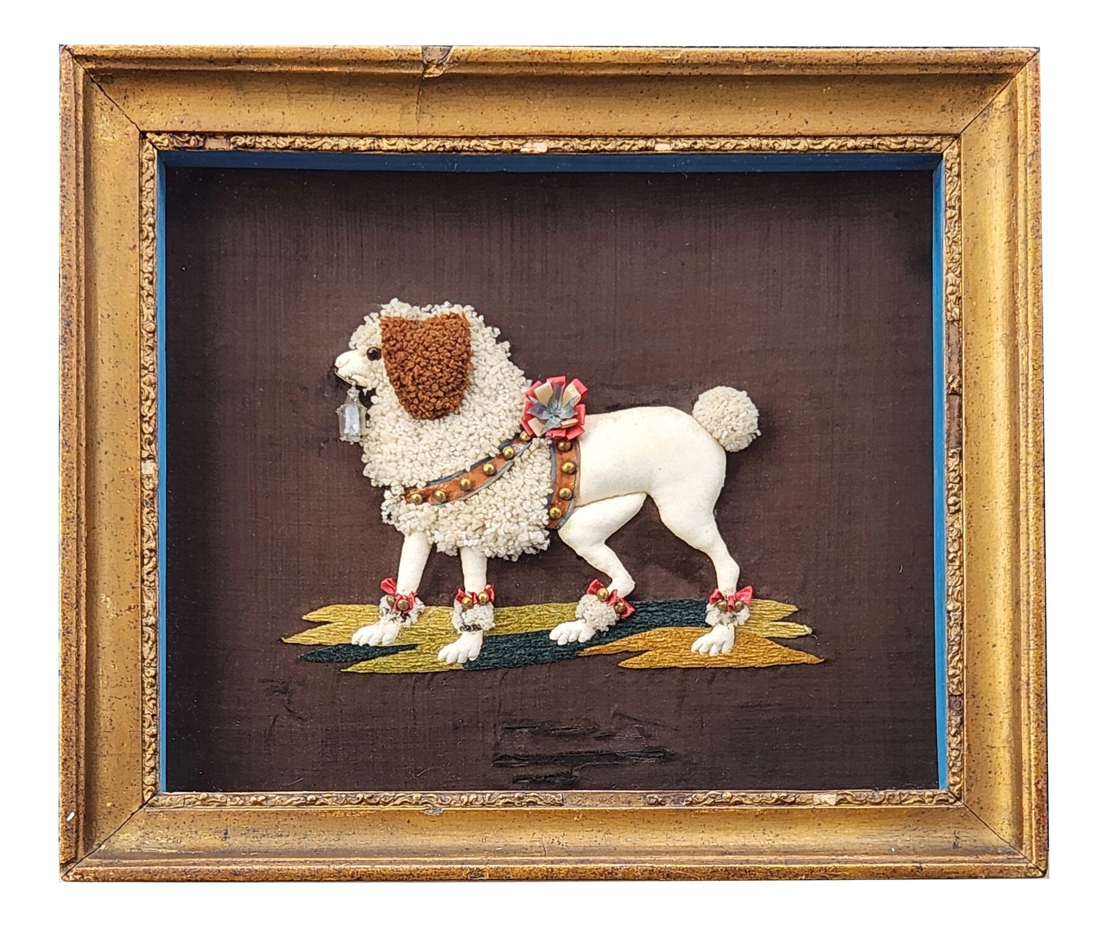 Framed Needlework of a Poodle with Decorative Harness and Gilt Frame: Framed needlework textile depicting a standing poodle adorned with a decorative harness, bows, and collar, executed in textured yarns and embroidery on a dark fabric ground. The dog is shown atop a st