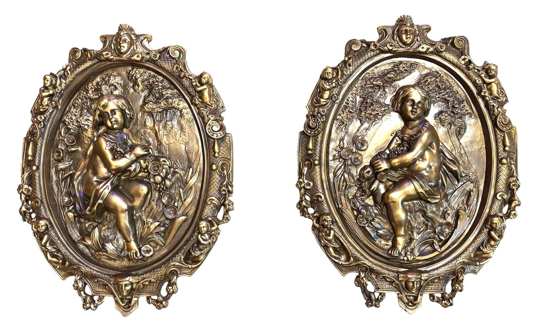 Pair of Antique Bronze Rococo Wall Plaques with High-Relief Putti Figures: Charming pair of antique cast bronze wall plaques featuring richly detailed rococo-style ornamentation and high-relief depictions of children in pastoral settings. Each oval plaque showcases a finely