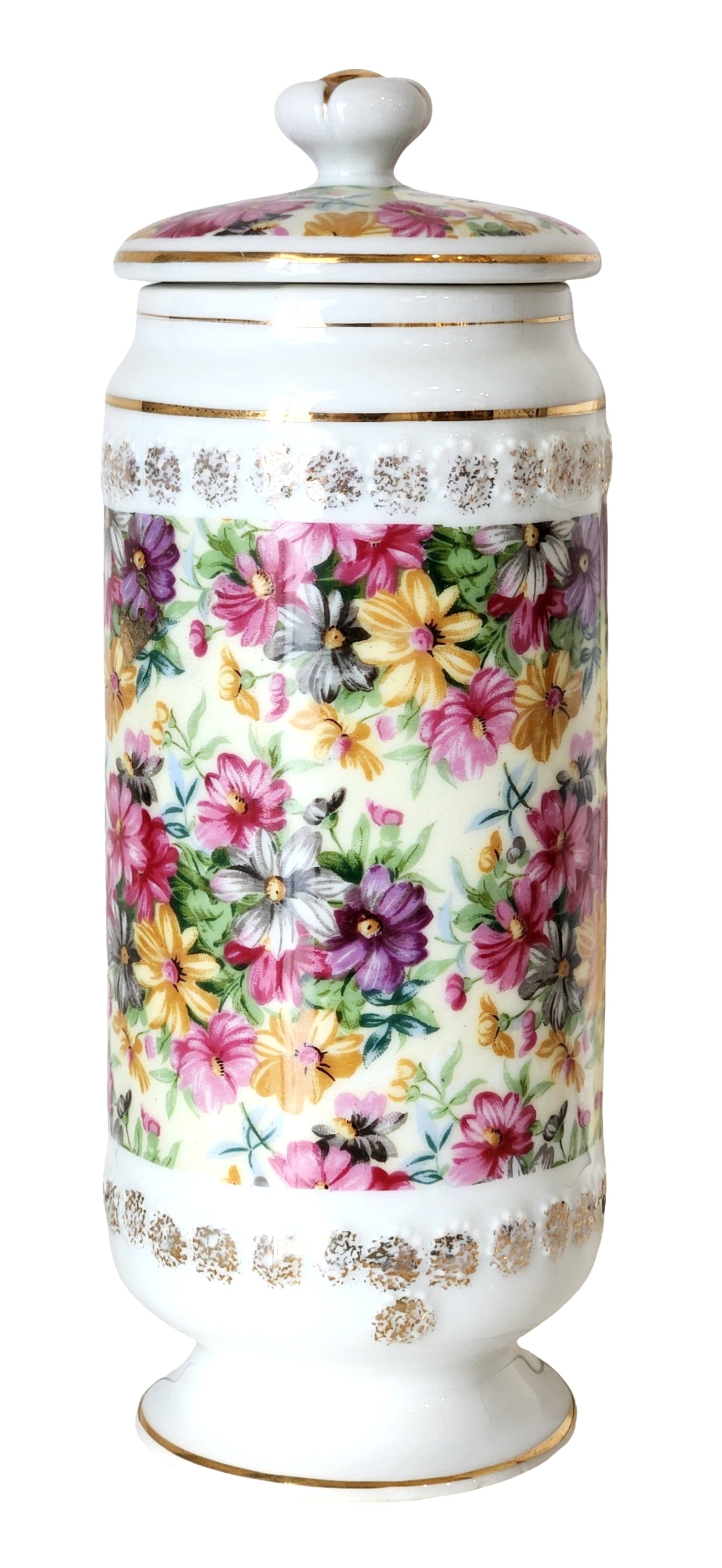 Porcelain Floral Lidded Jar / Canister with Gilt Decoration: Decorative porcelain lidded jar featuring a vibrant all-over floral design in pink, yellow, purple, and white blossoms set against a creamy white ground. The cylindrical body is framed by raised decor