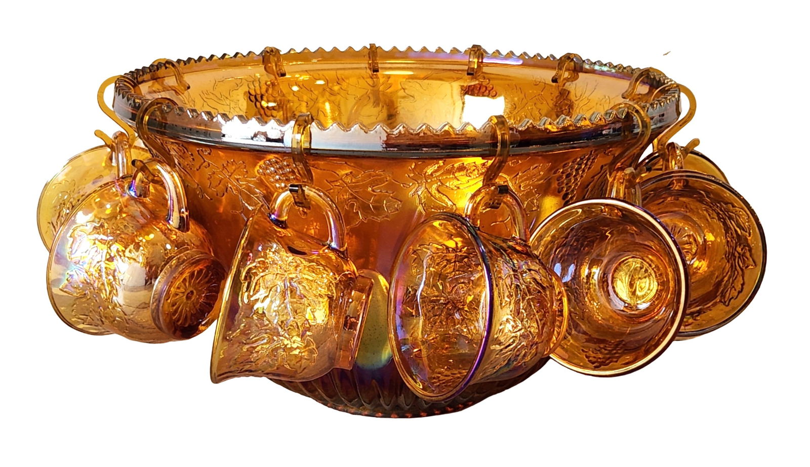 Amber Carnival Glass Punch Bowl Set with Matching Cups, Grape and Vine Pattern: A decorative amber carnival glass punch bowl set, comprising a large punch bowl and a collection of matching handled cups. The glass is moulded with a repeating grape and vine motif, enhanced by an