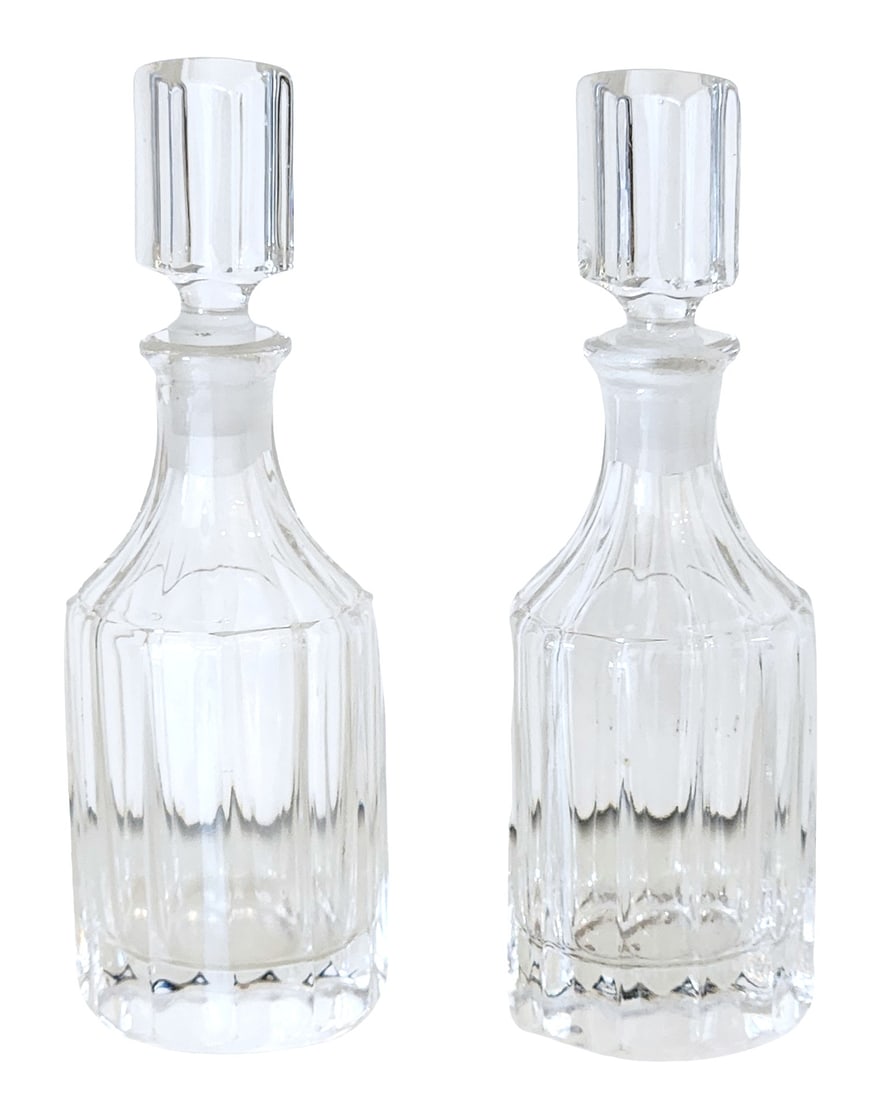 Pair of Cut Crystal Decanters with Stoppers: Elegant pair of clear cut crystal decanters, each with a faceted cylindrical body, paneled shoulders, and matching faceted stoppers. The decanters feature a heavy, star-cut base and a tall, tapered
