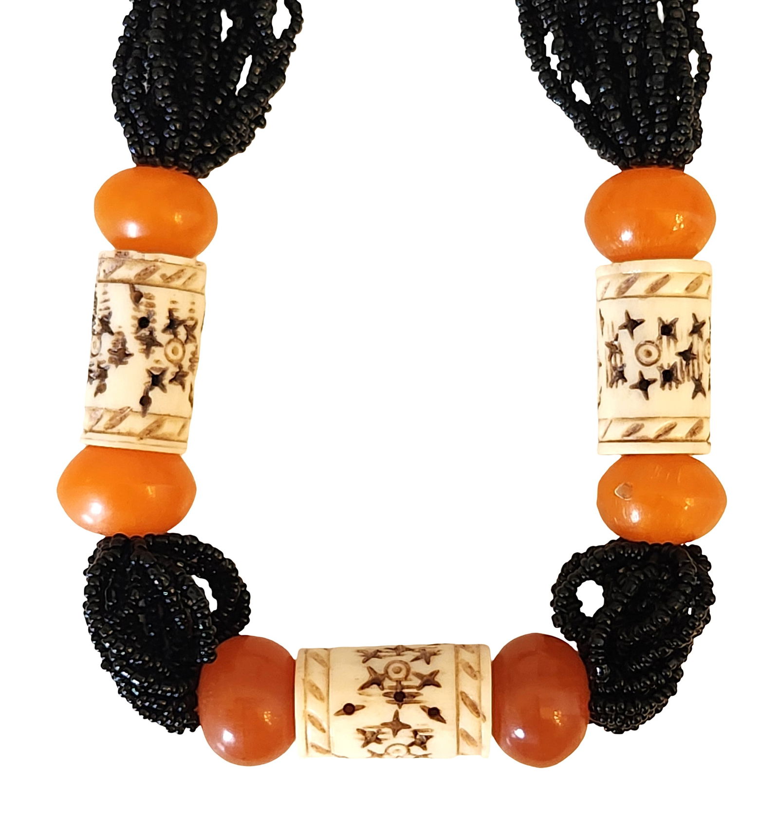 Vintage African Trade Bead Necklace with Carved Bone and Black Seed Beads: Striking vintage necklace composed of multiple strands of black seed beads accented with large carved bone beads and vibrant orange trade beads. The design features three cylindrical bone beads decora