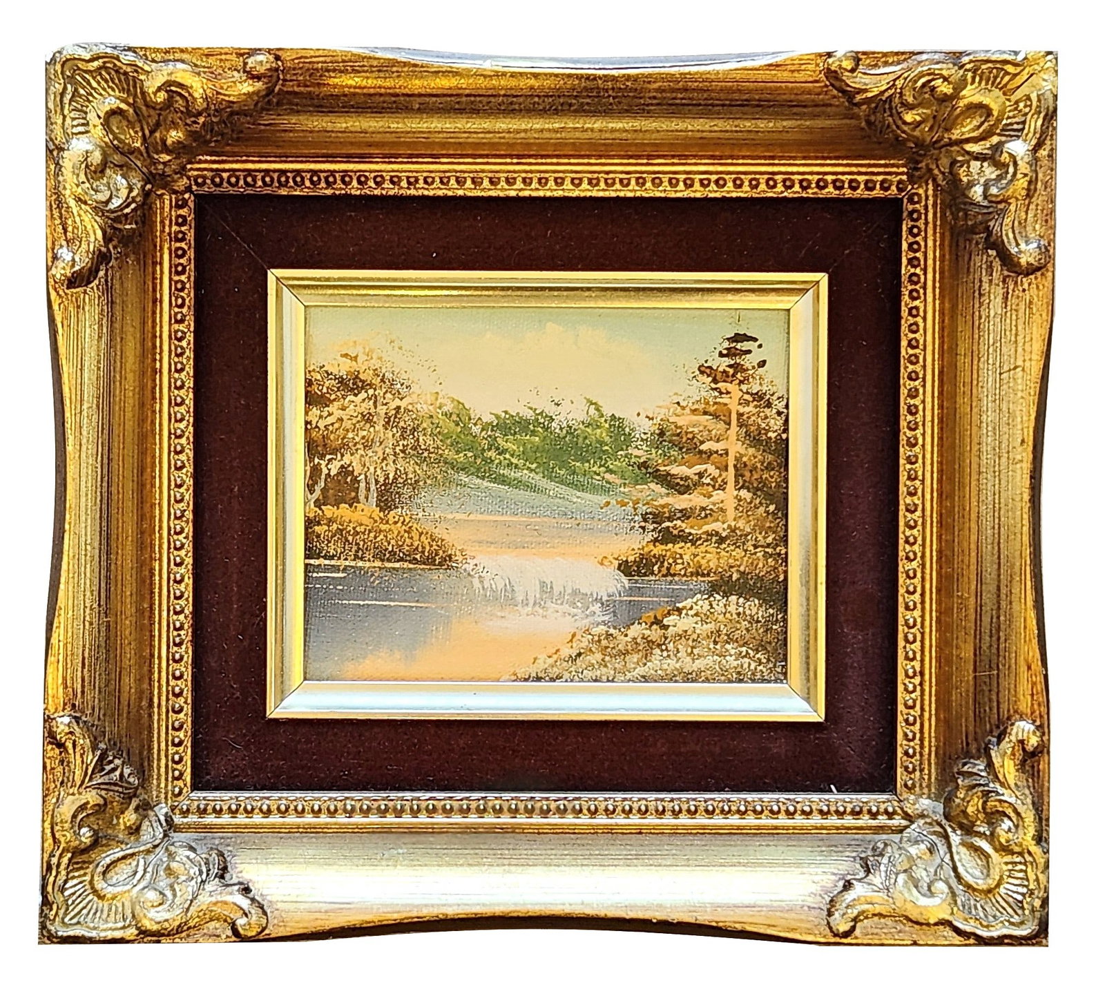 Vintage Landscape Painting in Ornate Gold Frame – Waterfall Lake Scene: Charming vintage landscape painting featuring a serene nature scene with a waterfall flowing into a calm lake surrounded by trees and foliage. The painting has a warm, impressionistic style with textu