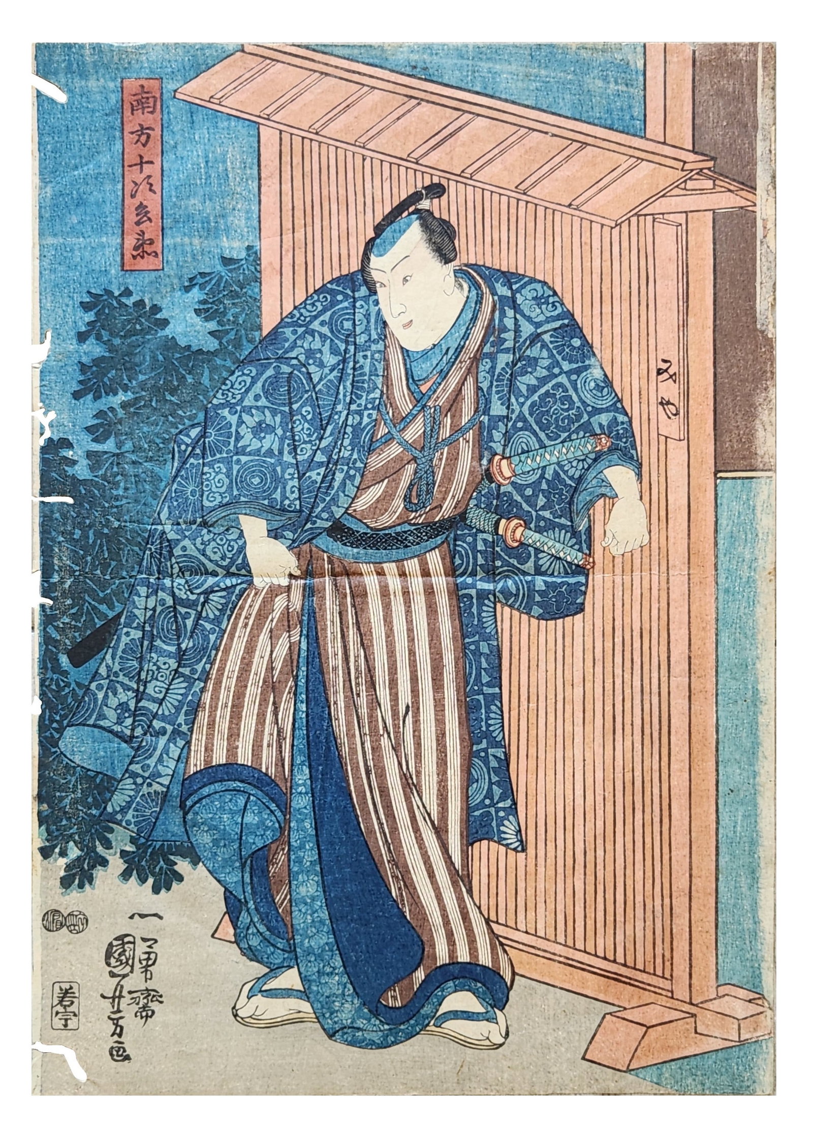 Japanese Woodblock Print of Samurai, Signed Kunisada (Utagawa School), Edo Period: Japanese ukiyo-e woodblock print depicting a standing samurai beside a wooden structure, dressed in a richly patterned blue kimono and striped hakama with two swords at his waist. The composition feat