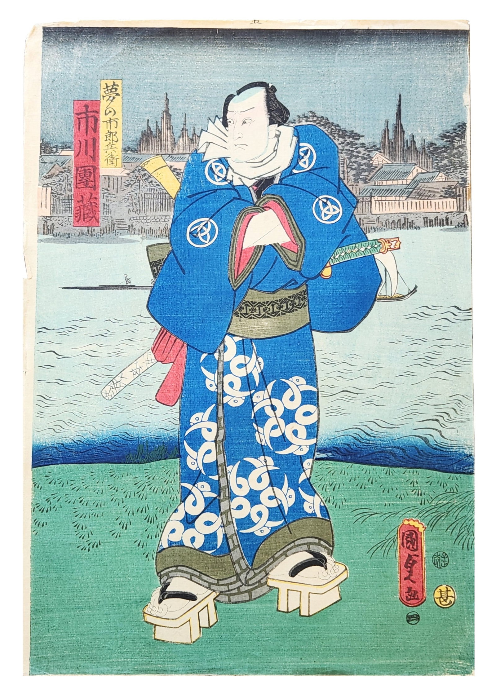 Japanese Ukiyo-e Kabuki Actor Woodblock Print, Utagawa Kunisada (Toyokuni III): A Japanese Ukiyo-e woodblock print depicting a Kabuki actor standing in a landscape setting near water with buildings and trees visible in the background. The figure wears a striking blue robe decorat