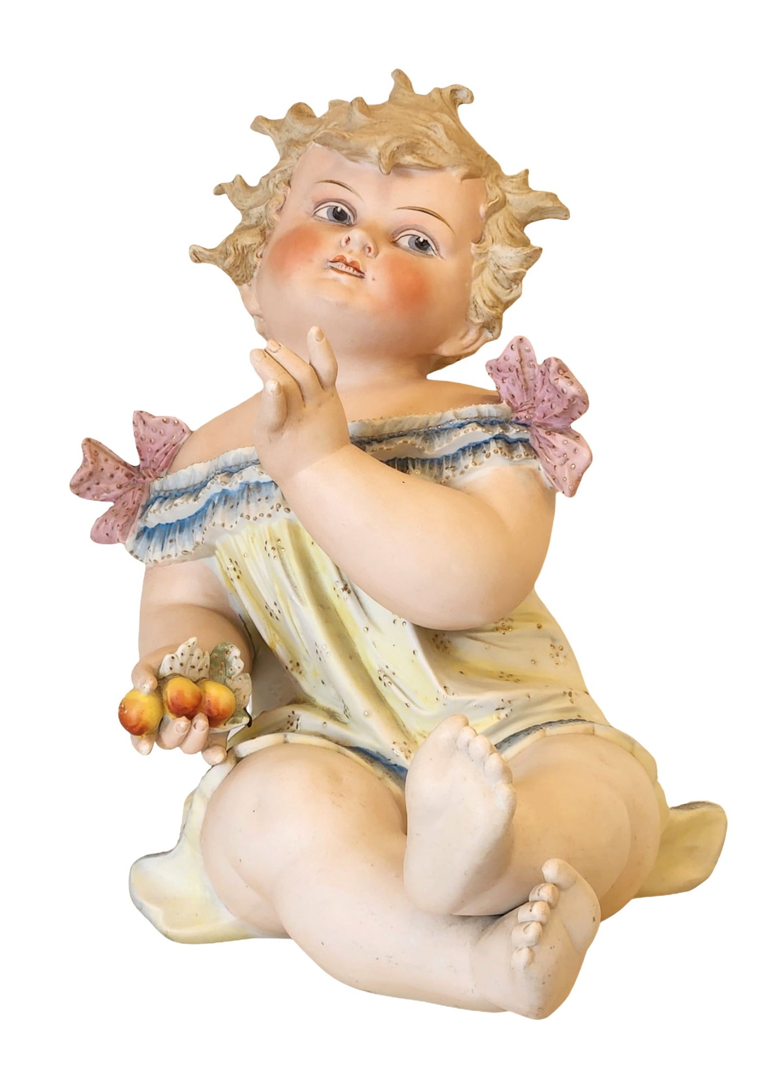 Large German Bisque Porcelain Figure of a Child with Fruits: Charming large German bisque porcelain figure depicting a seated child holding fruits, wearing a pastel yellow dress with blue trim and pink bows. The delicate modeling captures lifelike details and a