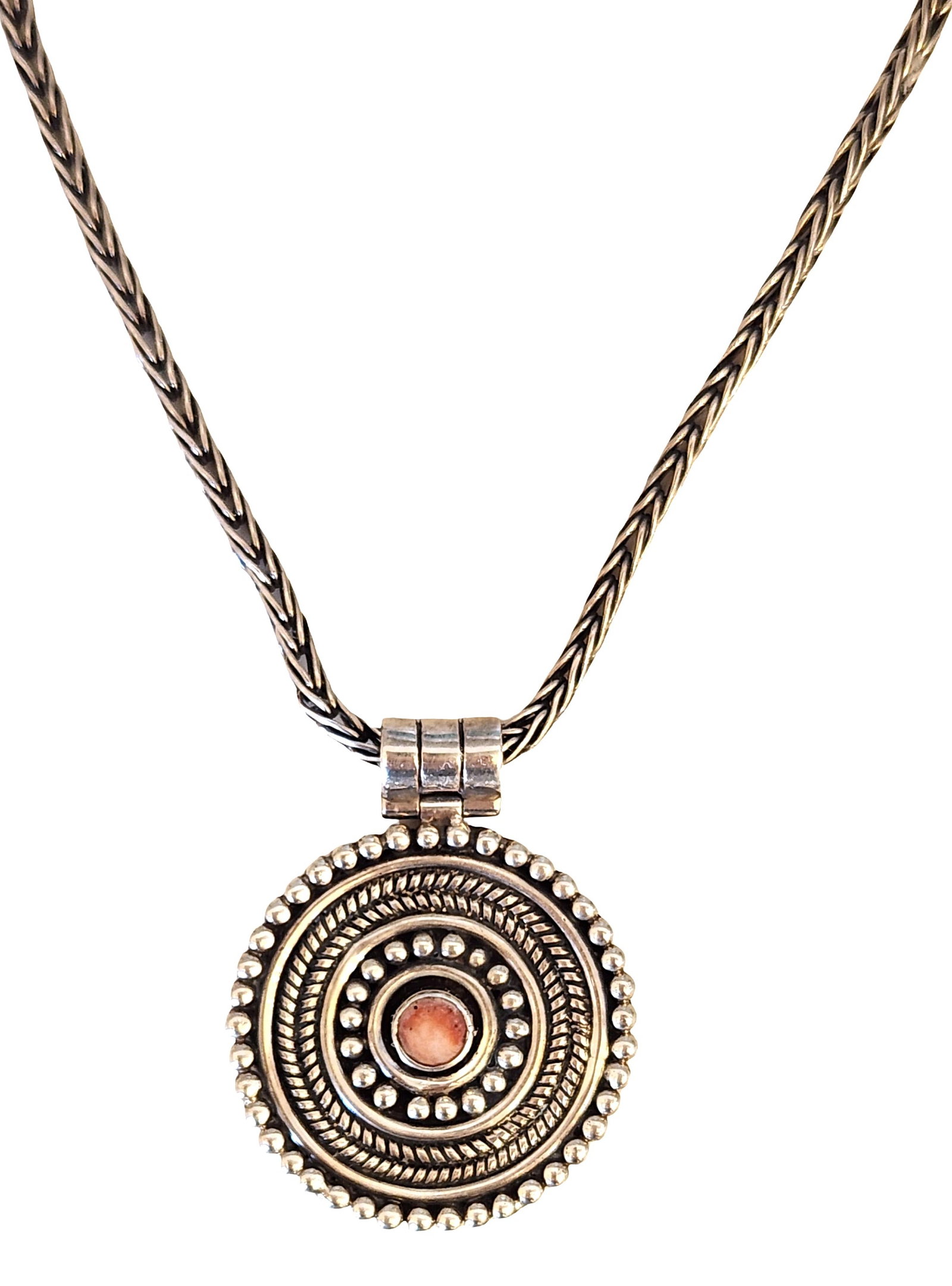 Ecuadorian Sterling Silver Pendant Necklace with Cabochon Accent: Sterling silver pendant necklace featuring a circular pendant with concentric rope-twist and beadwork detailing, centered with a small round cabochon accent of warm reddish tone. The pendant is suspen