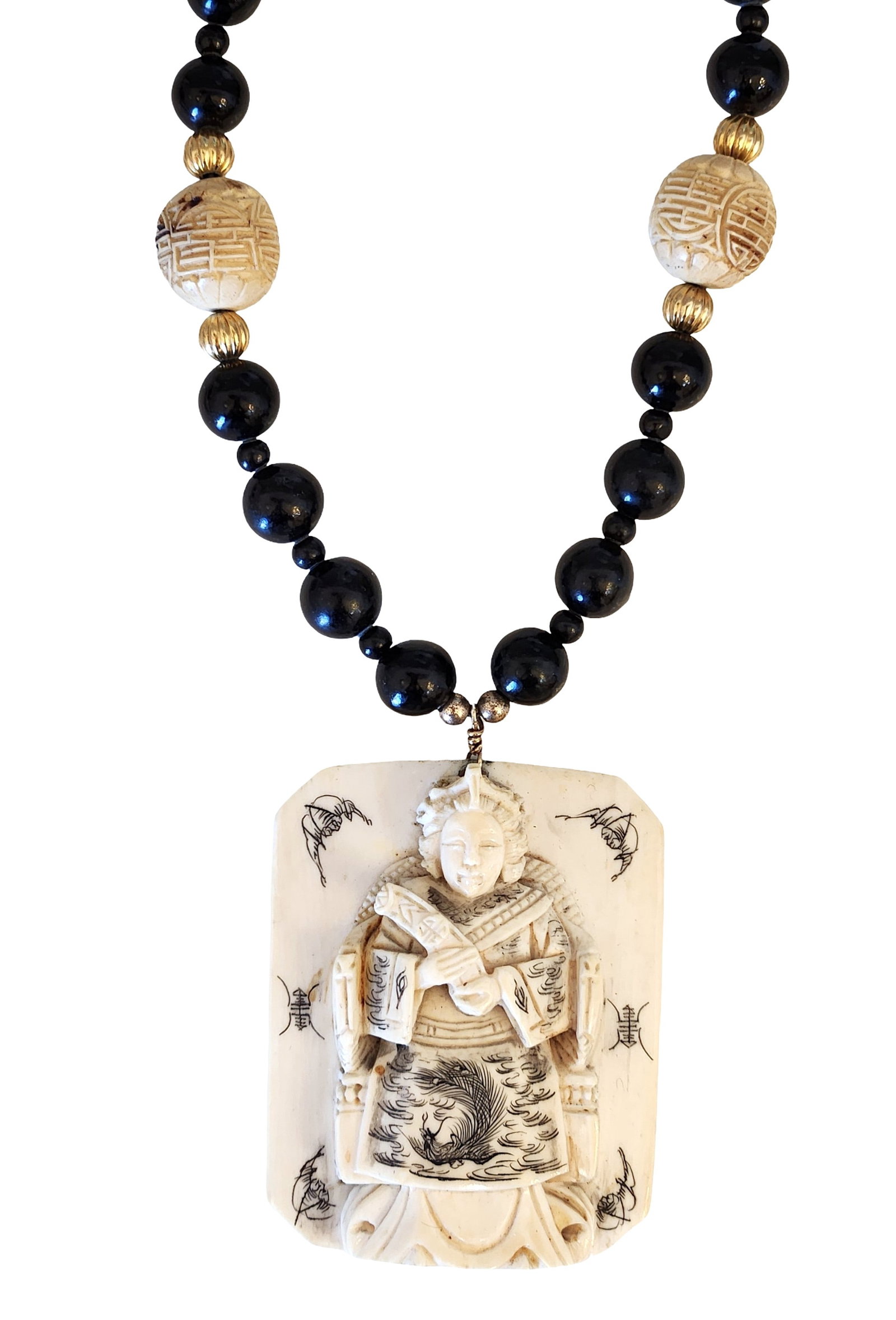 Carved Figural Pendant Necklace with Black Beads and Decorative Accents: Necklace featuring a carved rectangular figural pendant depicting a robed figure with incised decorative motifs on the front and symbolic markings on the reverse. The pendant is suspended from a stran
