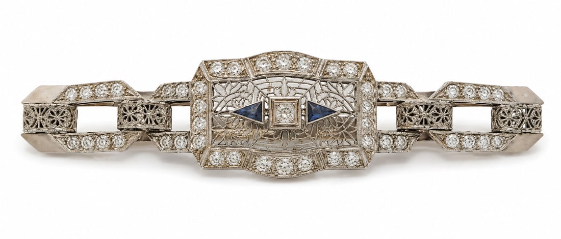 Art Deco Sterling Silver Filigree Bracelet with Blue Accents and Paste Stones: Art Deco style sterling silver bracelet featuring an openwork filigree design accented with clear paste stones and dark blue triangular accents. The central plaque is framed by geometric motifs and se