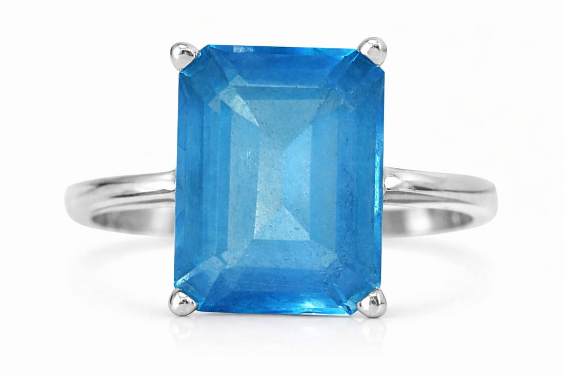14K White Gold Ring with Emerald-Cut Topaz: A 14K White Gold ring with a large rectangular, emerald-cut Topaz in a four-prong setting. The vivid blue stone displays a transparent body with visible inclusions and a step-cut faceting that enhance