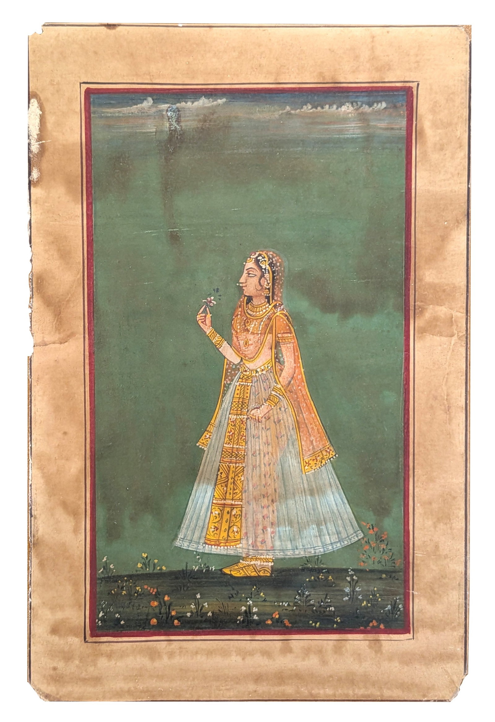 Indian Miniature Painting of a Noblewoman Holding a Blossom: Indian miniature painting depicting an elegantly dressed noblewoman standing in profile while delicately holding a small flowering sprig. She wears a finely detailed translucent skirt, an orange veil,