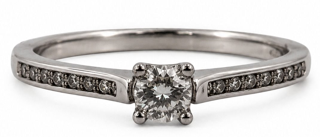 10K White Gold Diamond Solitaire Engagement Ring: Crafted in 10K white gold, this engagement ring features a round brilliant cut center diamond in a four prong setting, accented by additional round diamonds channel-set along the shoulders of the band