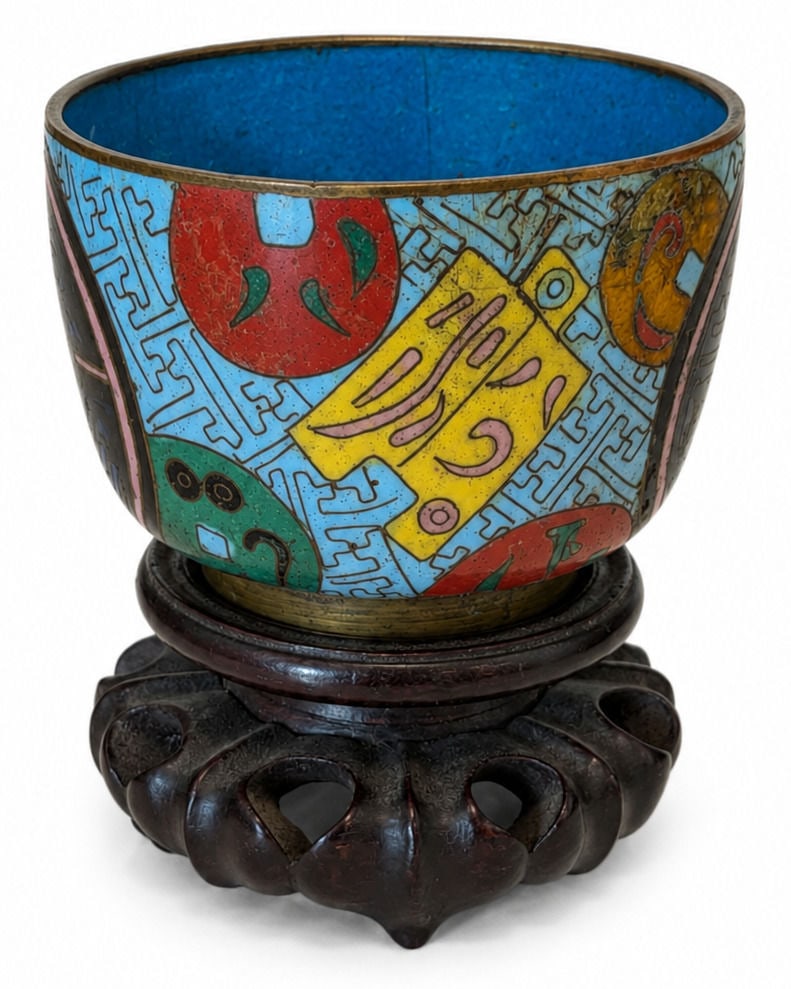 Chinese Cloisonne Enamel Bowl with Carved Wooden Stand: A small Chinese cloisonne enamel bowl featuring a tapered circular form decorated with colorful stylized motifs and geometric patterns in turquoise, yellow, red, green, black, and pink enamel separate