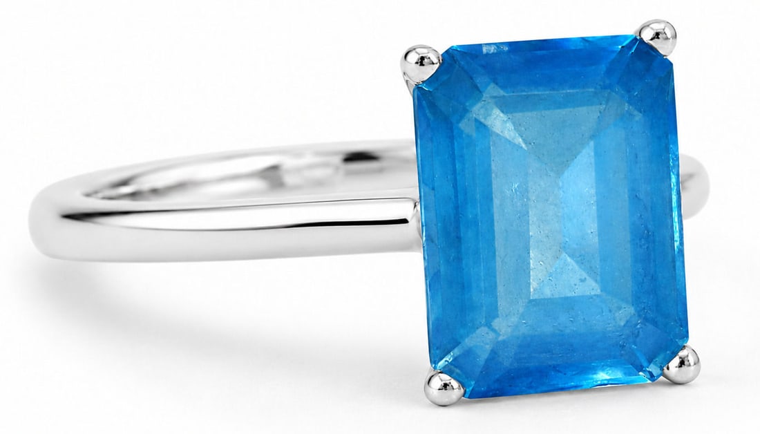 14K White Gold Ring with Emerald-Cut Topaz: A 14K White Gold ring with a large rectangular, emerald-cut Topaz in a four-prong setting. The vivid blue stone displays a transparent body with visible inclusions and a step-cut faceting that enhance