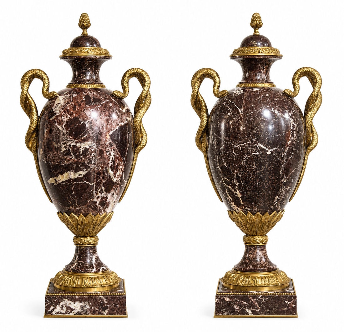 Pair of Neoclassical Rouge Marble & Gilt Bronze Covered Urns with Serpent Handles: A magnificent pair of neoclassical covered urns crafted in richly veined rouge marble, each adorned with finely cast gilt-bronze serpent handles that coil gracefully along the sides. The urns feature 