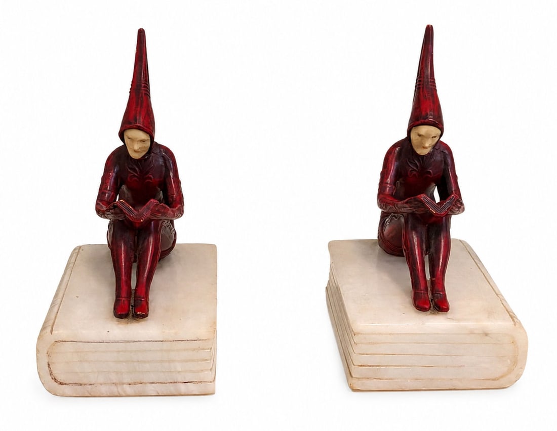 Pair of Art Deco Cold-Painted Bronze & Carved Bone Pixie Bookends: A charming pair of Art Deco bookends featuring seated pixie or jester figures perched atop carved alabaster or marble bases shaped like closed books. Each figure is rendered in cold-painted deep