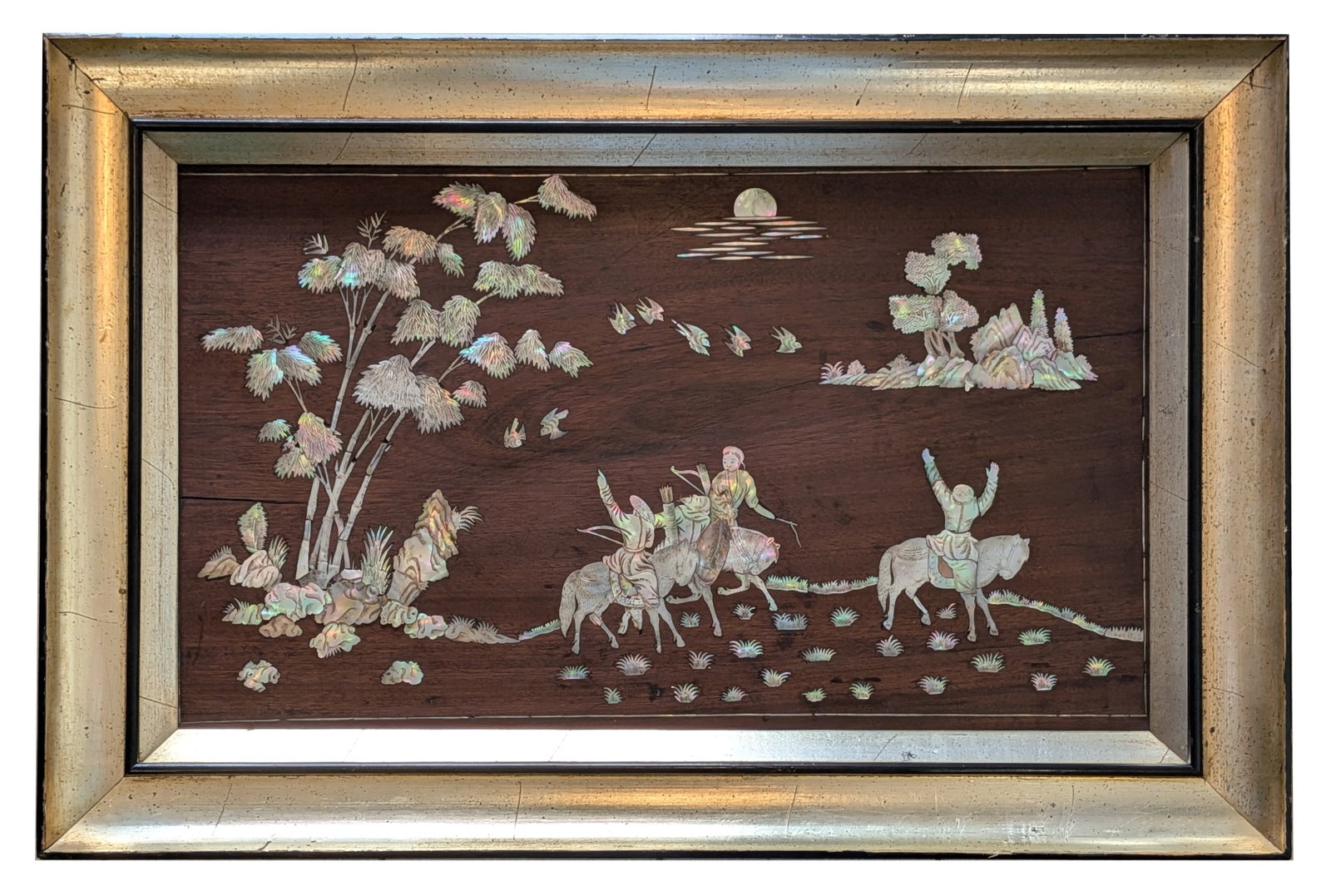 Chinese Mother of Pearl Inlaid Hardwood Panel in Gilt Frame: Decorative Chinese hardwood panel finely inlaid with shimmering mother of pearl depicting a tranquil landscape with three mounted figures traveling beneath flowering trees, accompanied by birds in fli