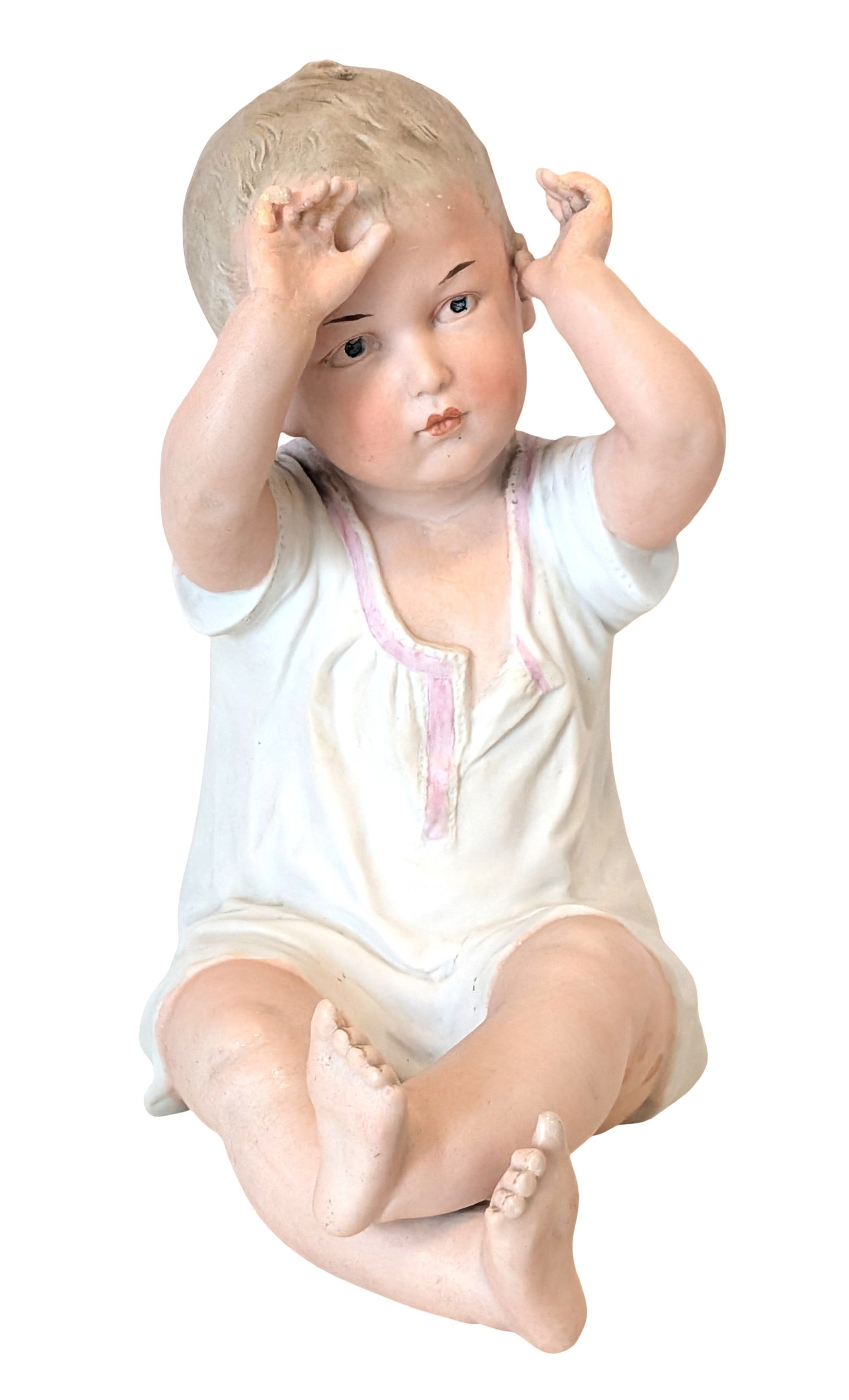 Heubach Piano Baby German Bisque Figure, Early 20th Century: Modeled as a seated infant in a white romper with pink trim, raising both hands toward its head. Finely painted facial features with blue eyes and naturalistic flesh tones. Underside with blue undergl