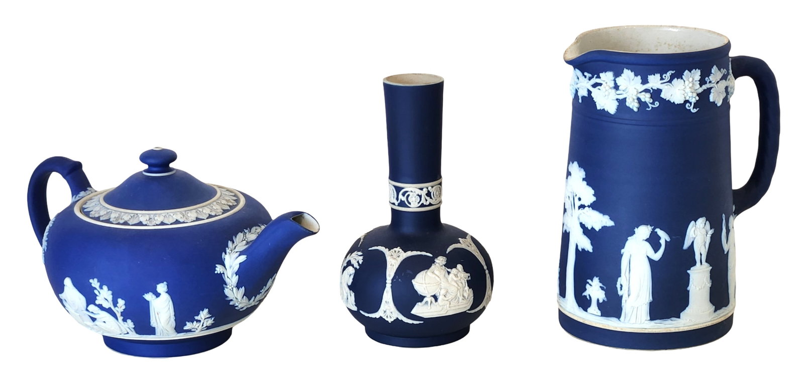 Three Wedgwood Jasperware Blue and White Pieces: Teapot, Jug, and Bottle Vase: Group of three Wedgwood jasperware items in the classic cobalt blue ground with applied white relief decoration, comprising a teapot with cover, a tall bottle-form vase, and a jug Each piece is decora