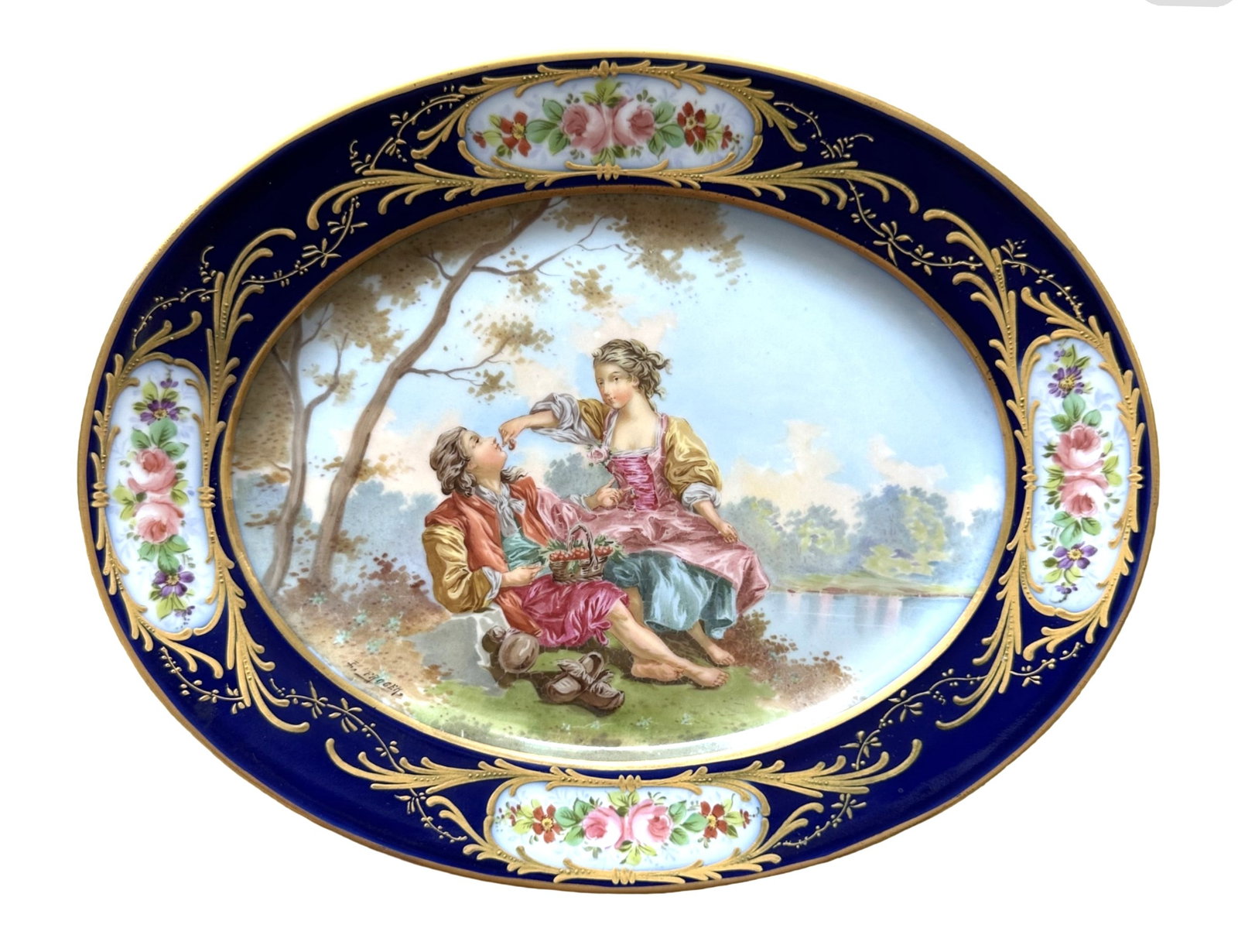 19th Century Sevres Hand-Painted Oval Porcelain Plate with Courting Scene: Elegant 19th century Sevres oval porcelain plate featuring a finely hand-painted Rococo scene of a courting couple seated beneath a tree beside a lake. The central image is framed by a deep cobalt blu