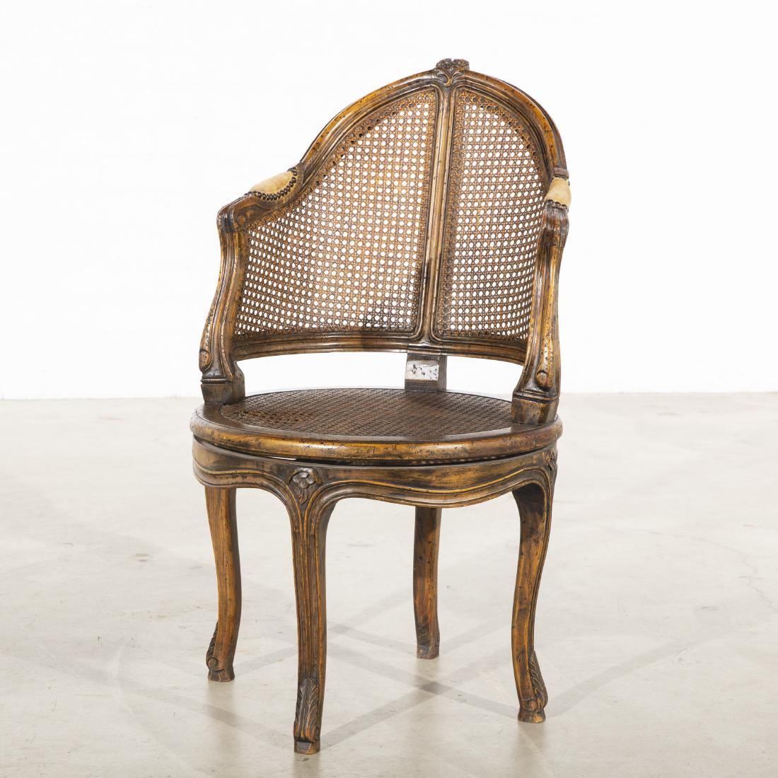 A Louis XV style caned corner bergere: A Louis XV style carved beechwood and cane paneled revolving bergÃ¨re 20th century height 36 3/4in (93.5cm); width 21 1/4in (54cm); depth of seat 19in (48cm)