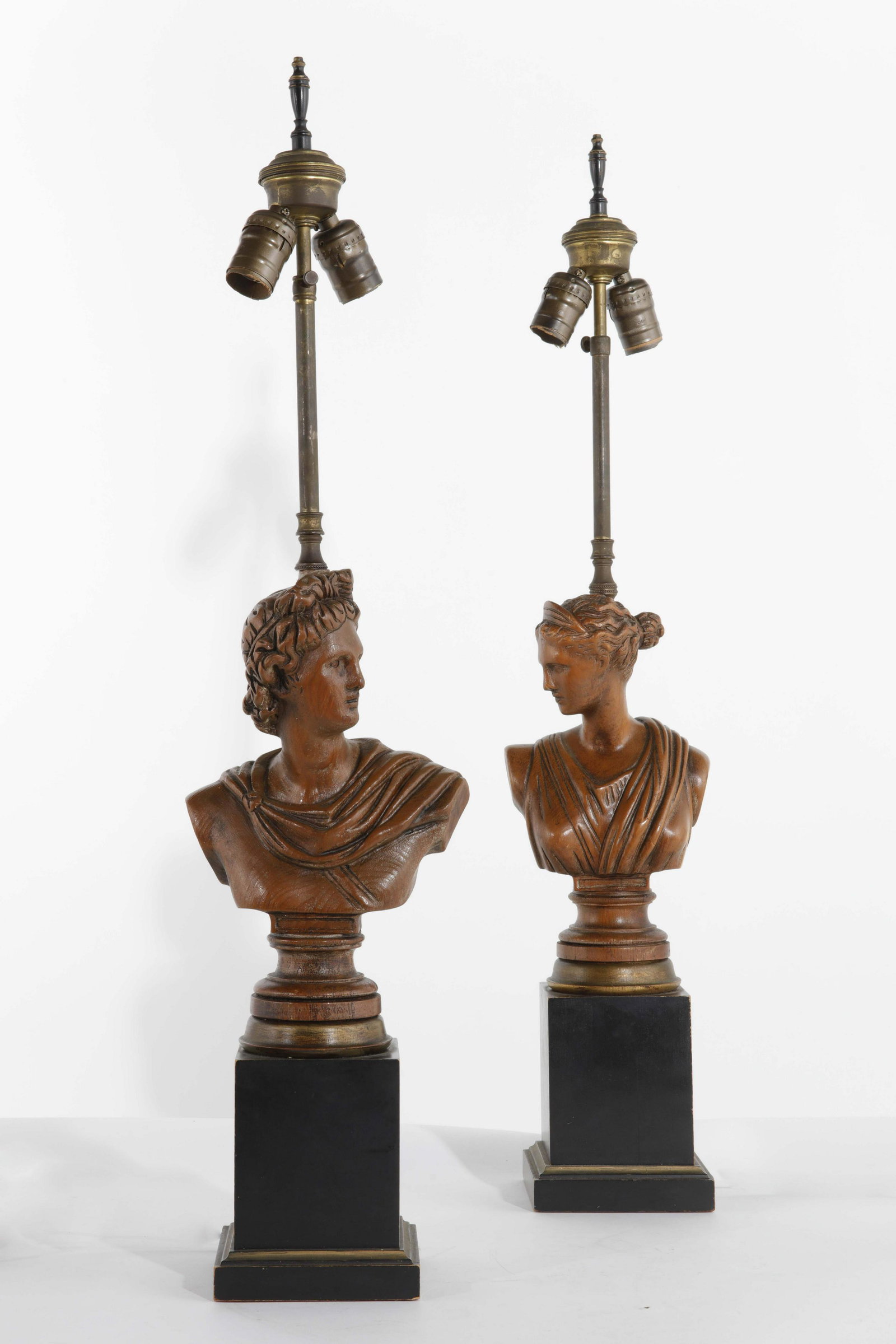 A pair of wood bust form table lamps: A pair of wood bust form table lamps raised on ebonized plinths 20th century height to finial 31 1/4in (79.5cm)Provenance: Property from The McNally Company Antiques, Rancho Santa Fe, California.