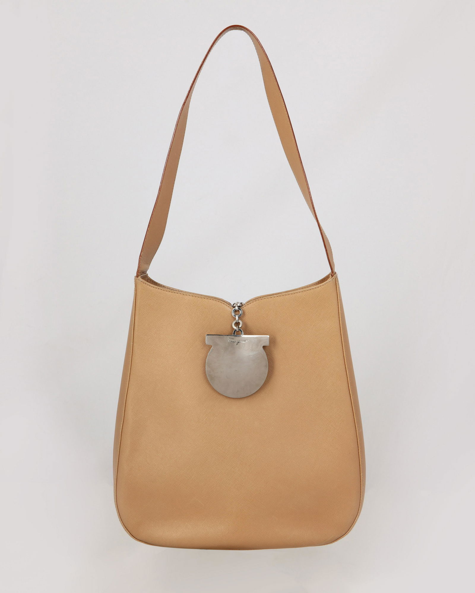 A Ferragamo tan leather shoulder bag: A Ferragamo tan leather shoulder bag Oval shape with single strap and back zipper Ferragamo icon chrome medallion and chain pull as front closure. Interior with black lining and an open pocket and a z