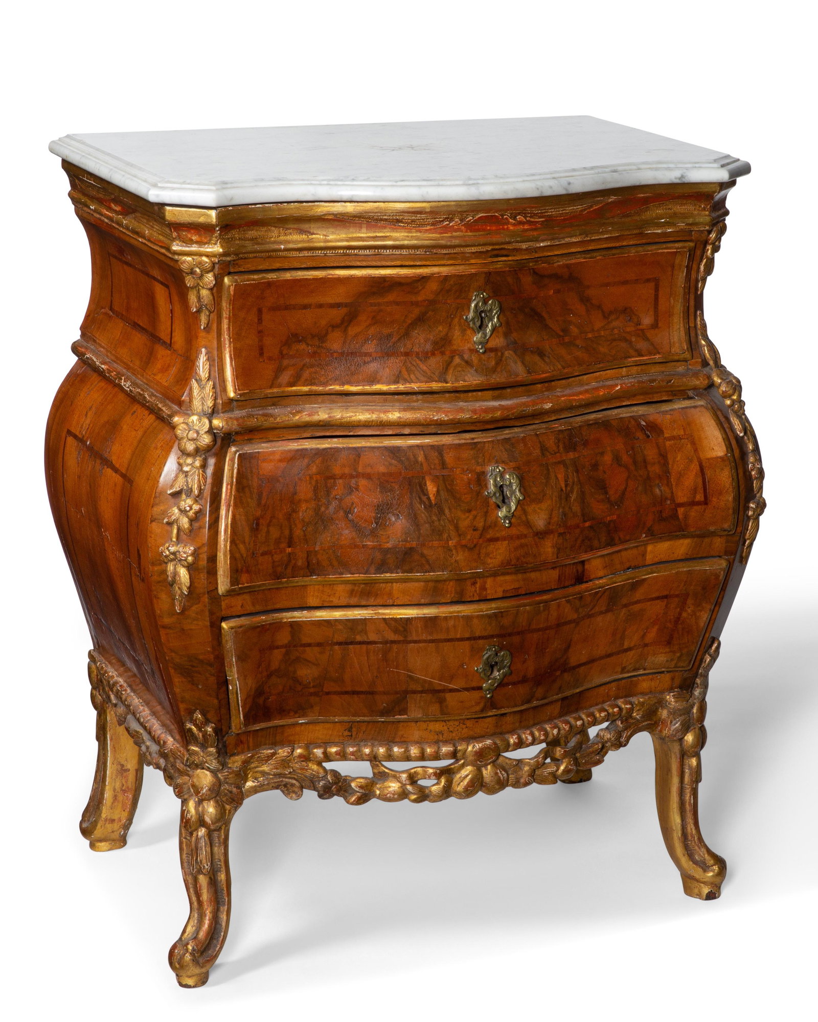 A Danish Rococo walnut bombe commode, Orttmann: A diminutive Danish Rococo parcel gilt walnut bombe commode in the manner of Matthias Orttmann mid 18th century Surmounted by a later veined white marble top. height 30 1/2in (77.5cm); width 25 3/4in 