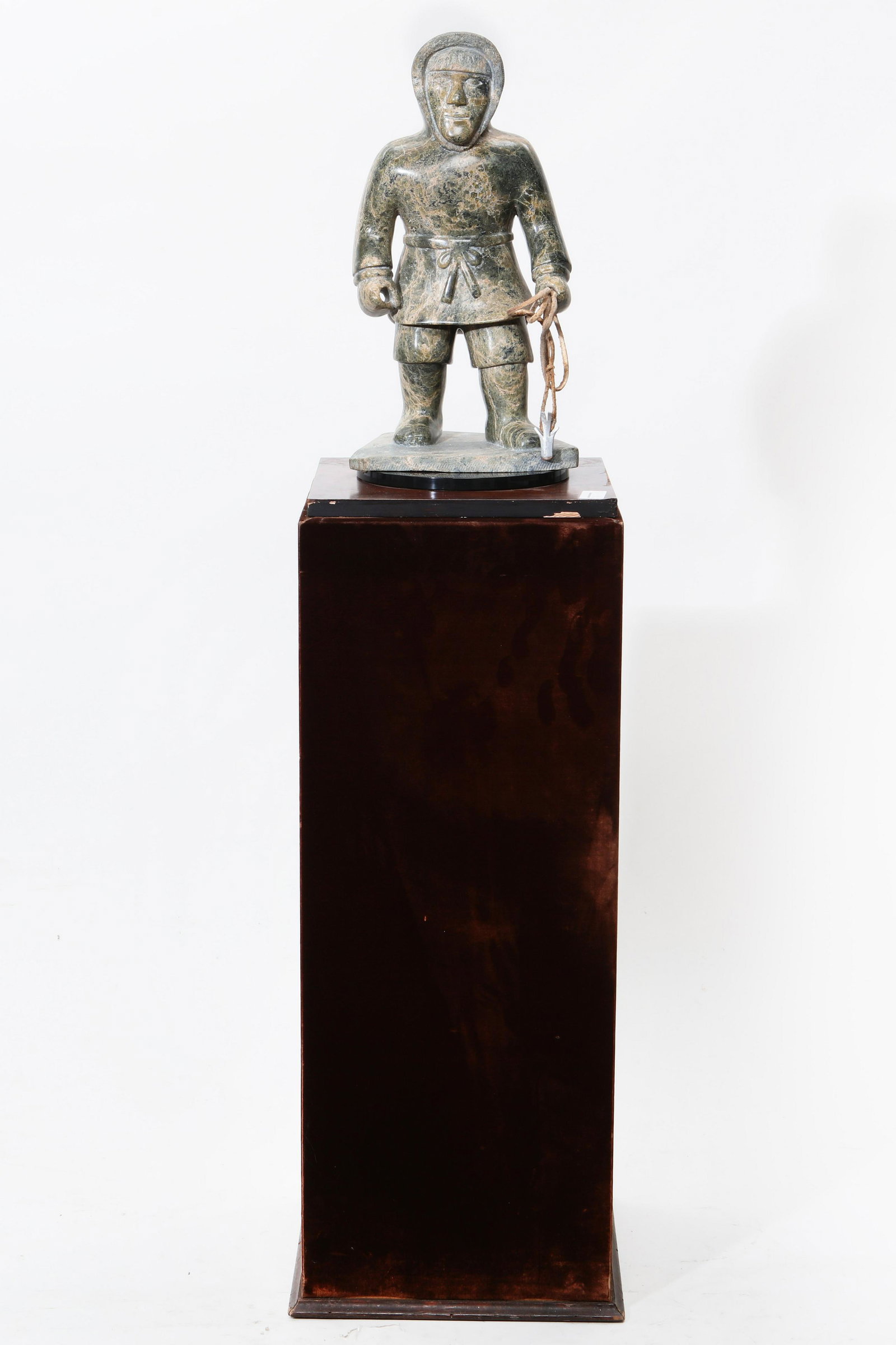 A carved hardstone figure of an Eskimo: A carved hardstone figure of an Eskimo Raised on a velvet upholstered pedestal. height of figure 18in (46cm); height overall 54in (137cm) Provenance: Property from the Collection of Edward and Mildred