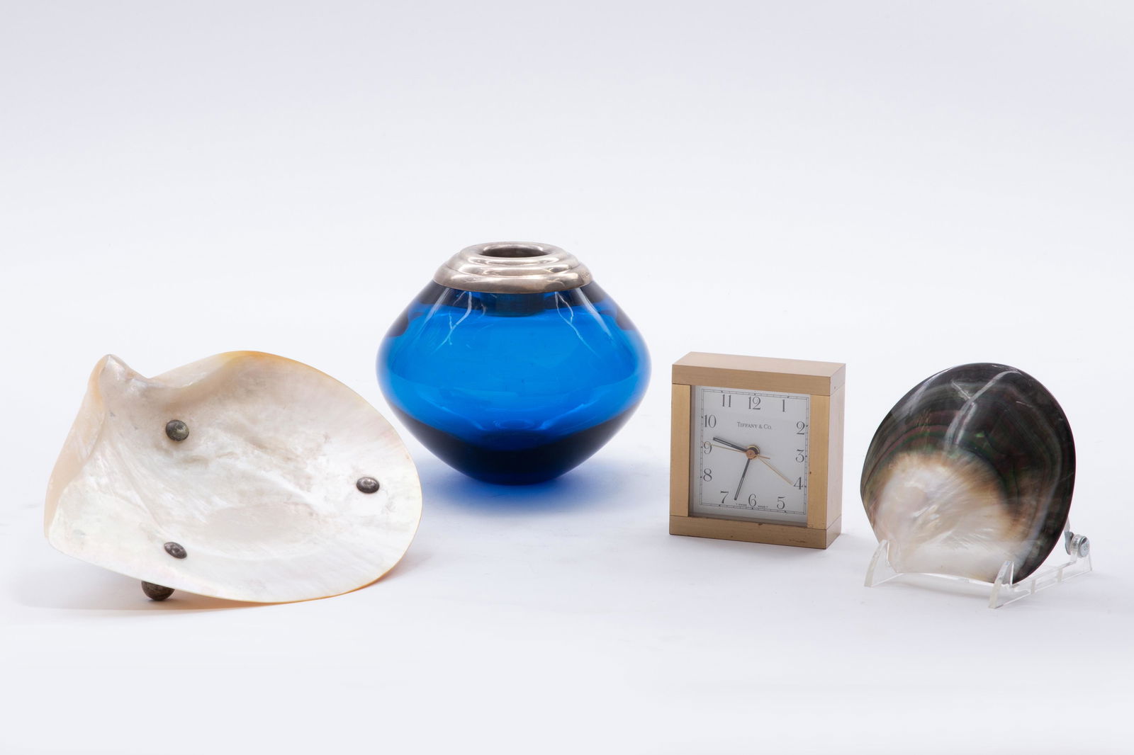 A group of four table decorations, Tiffany: A group of four table decorations 20th century Comprising a Tiffany desk clock, two shell bowls and a glass and silver match striker. the match striker height 5in (12.75cm); width 5 1/2in (14xm) Prove