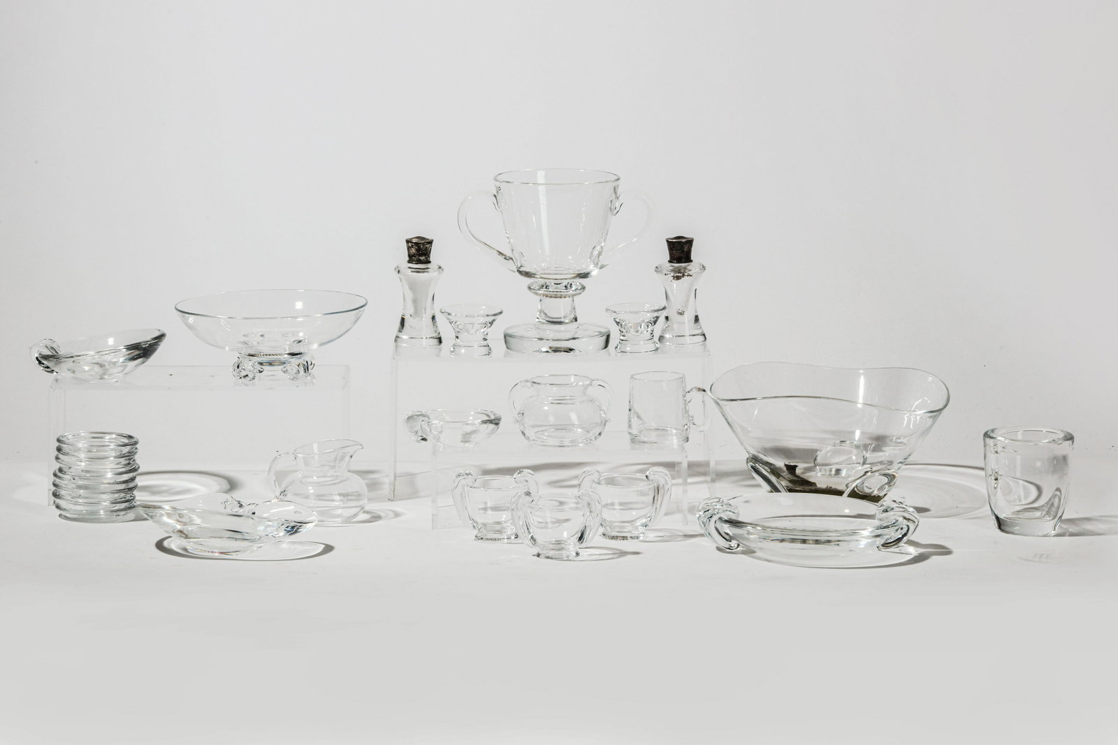 A 25 pc suite of Steuben clear glass tableware: A suite of Steuben clear glass tableware mid-20th century Comprising a trefoil/Clover (8040), a bowl on four scroll feet, a two handled vase/trophy, (7777), four ashtrays of various sizes, eight indiv