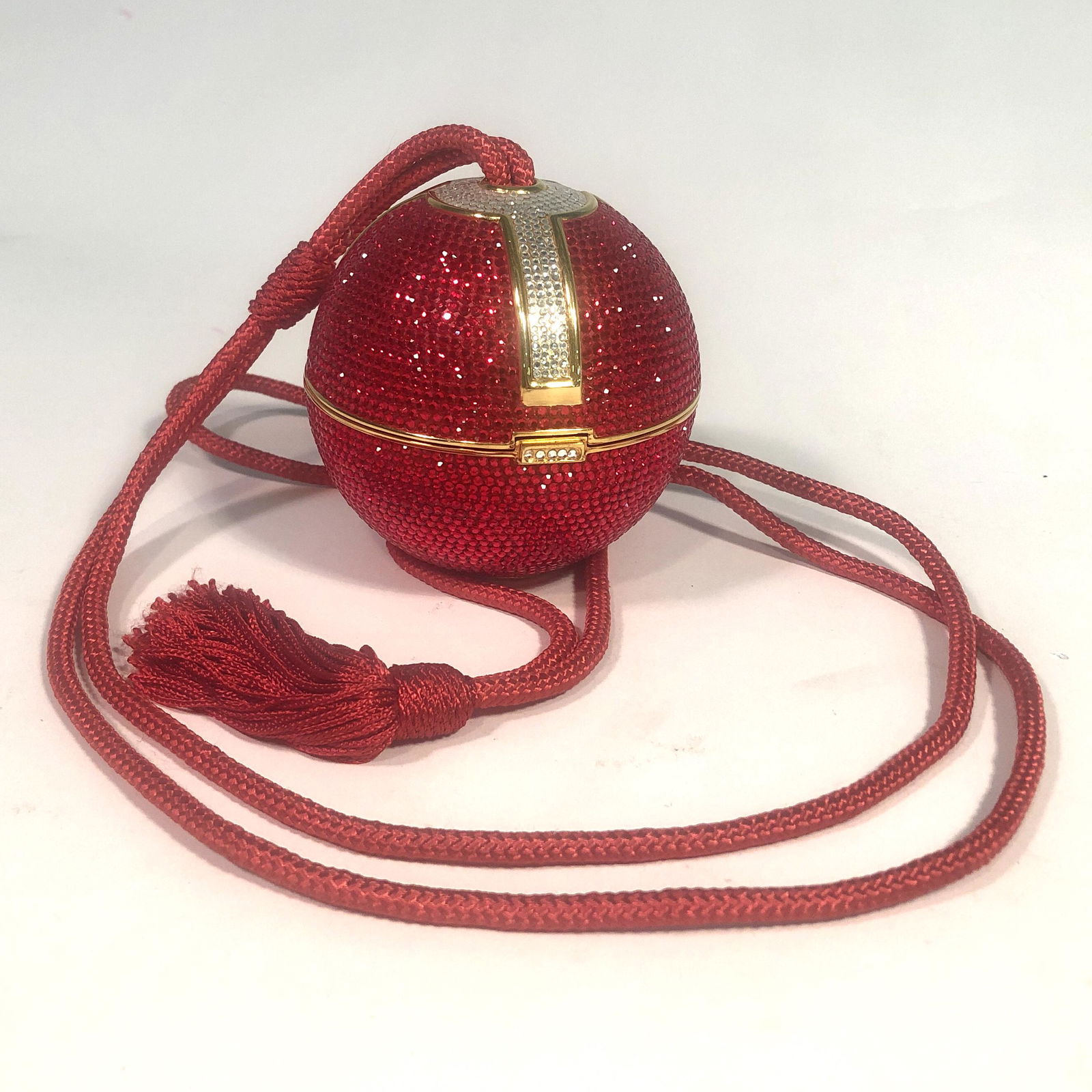 A Judith Leiber orb form minaudiere: A Judith Leiber orb form minaudiere The interior lined in metallic leather, with red cord shoulder strap and tassel, comb and mirror, applied factory label and stamped rim. diameter 3 1/2in (9cm)Prove