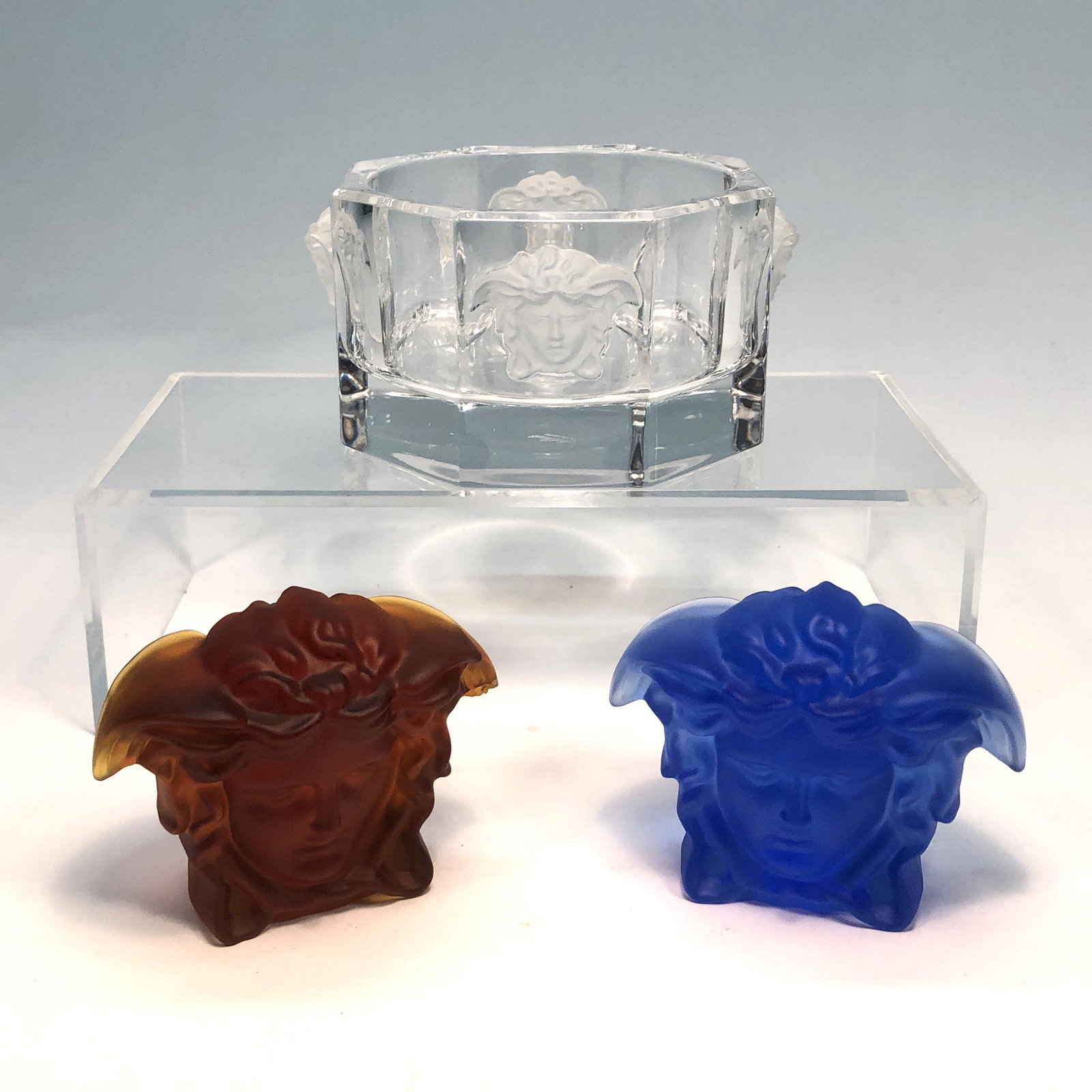 A Versace Medusa ashtray and paperweights: A Versace for Rosenthal frosted and clear glass Medusa Ashtray and two colored glass Medusa paperweights Each with etched factory mark and VERSACE. height of ashtray 3 1/8in (8cm); width 6in (15cm); h
