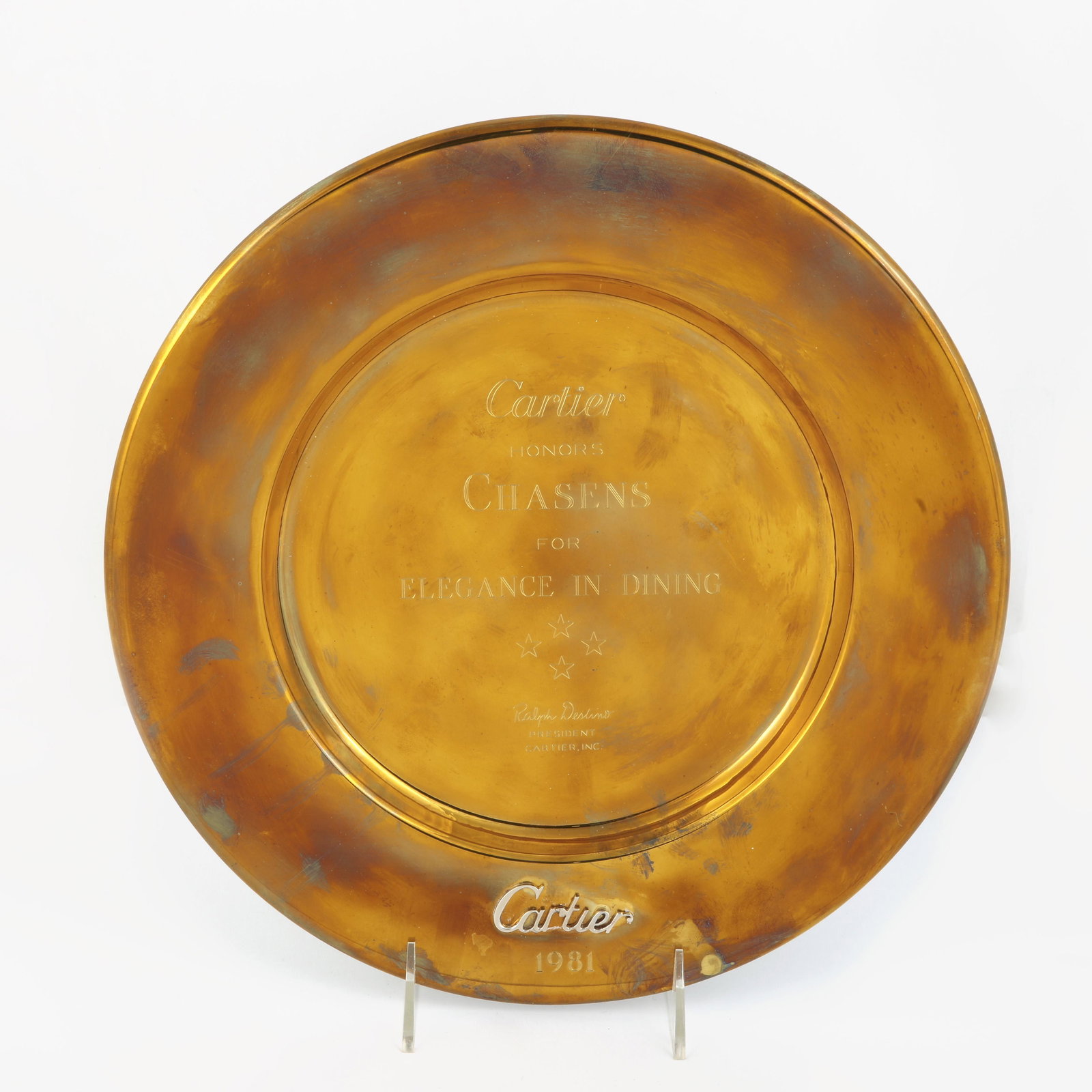 A gilt presentation plate to Chasens dated 1981: A gilt presentation plate to Chasens dated 1981 Inscribed Cartier honors Chasens for Elegance in Dining, 4 stars, Ralph Destino, President, Cartier.Inc.with applied Cartier label and dated 1981 to low