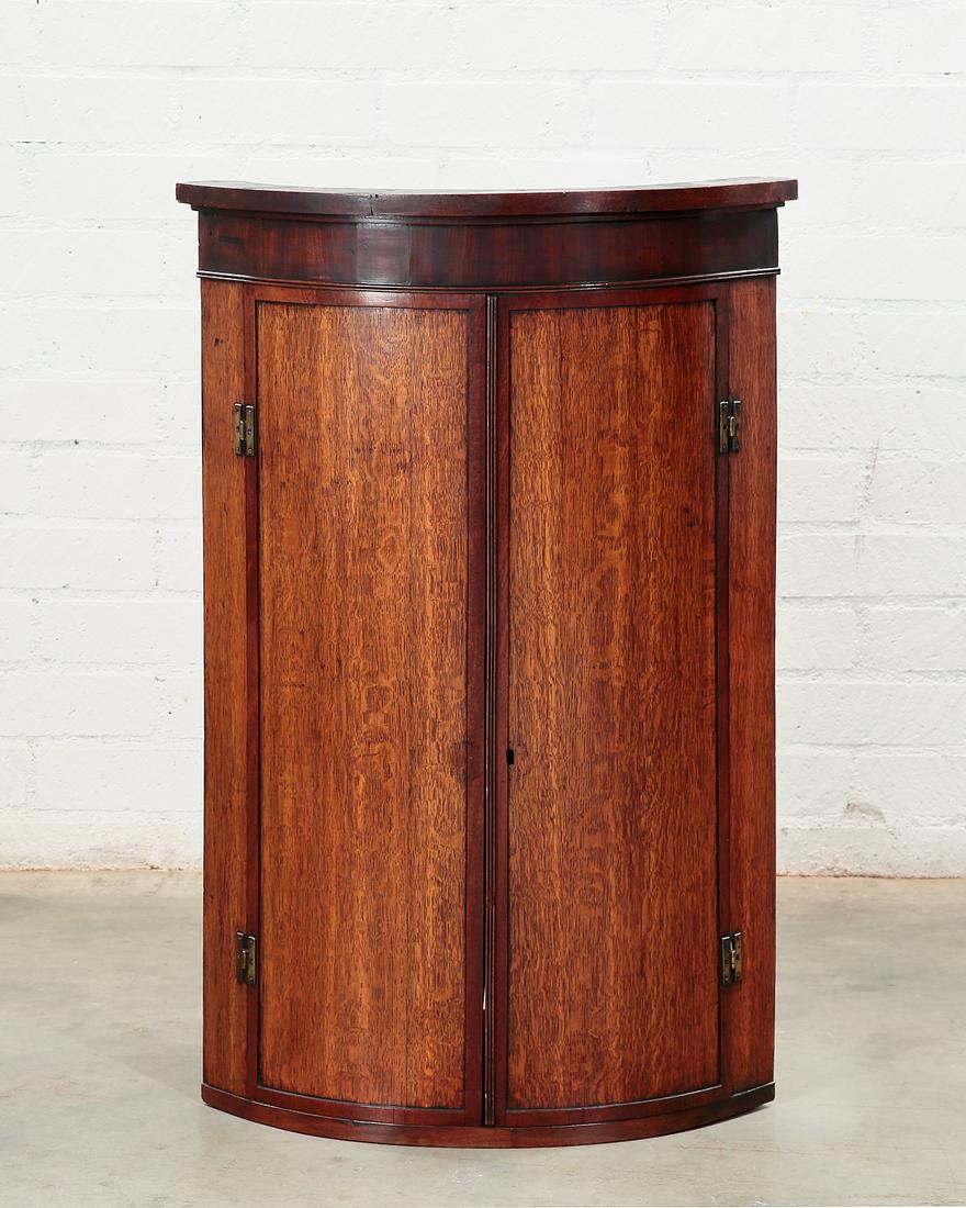 A George III oak and mahogany corner cupboard: A George III oak and mahogany bow front hanging corner cupboard late 18th century Fitted with three interior shelves. height 39 1/4in (99.5cm); width 25 1/4in (61.5cm); depth 18 1/2in (47cm) Provenanc