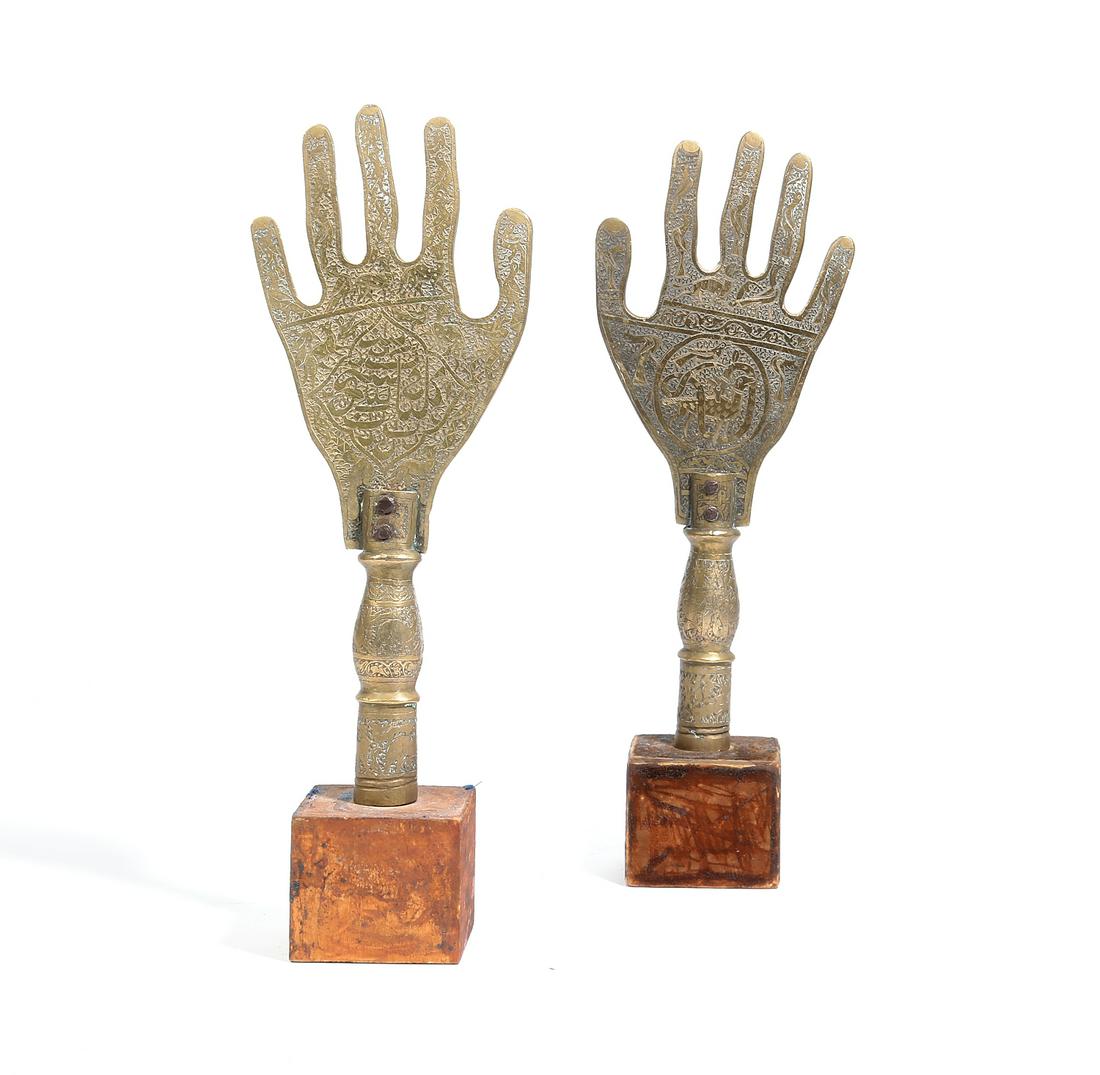 Middle Eastern brass standards, Hand of Fatima: A pair of Middle Eastern brass religious standards, in the form of the Hand of Fatima Each heavily decorated and with inscriptions, both raised on a small wood base. height of brass hand 13in (33cm); 