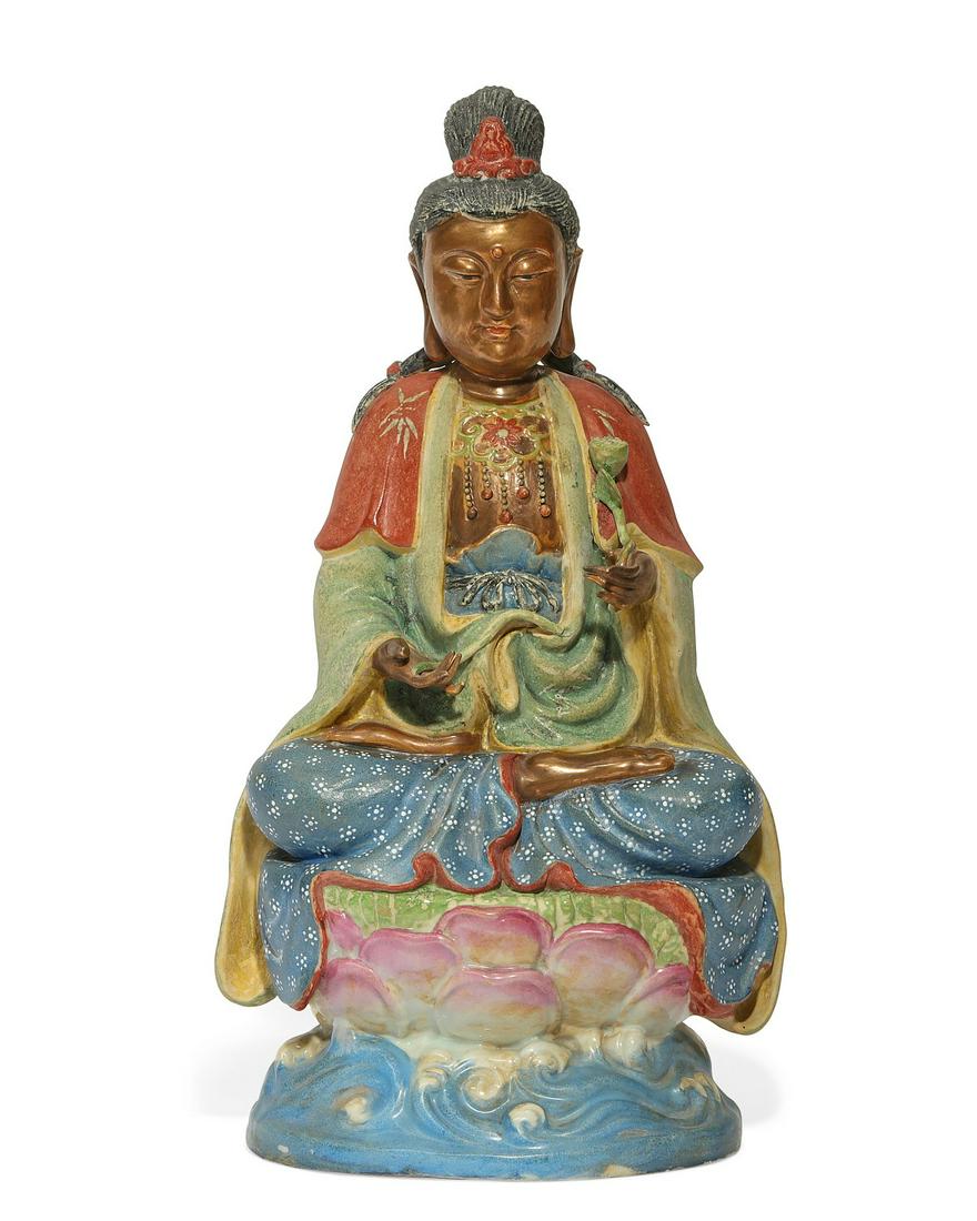 A Chinese seated porcelain model of Guanyin: A Chinese polychromed enameled seated porcelain model of Guanyin The seated and traditionally and colorfully attired bodhisattva raised upon an elaborate lotus and wave plinth holding the remnants of 