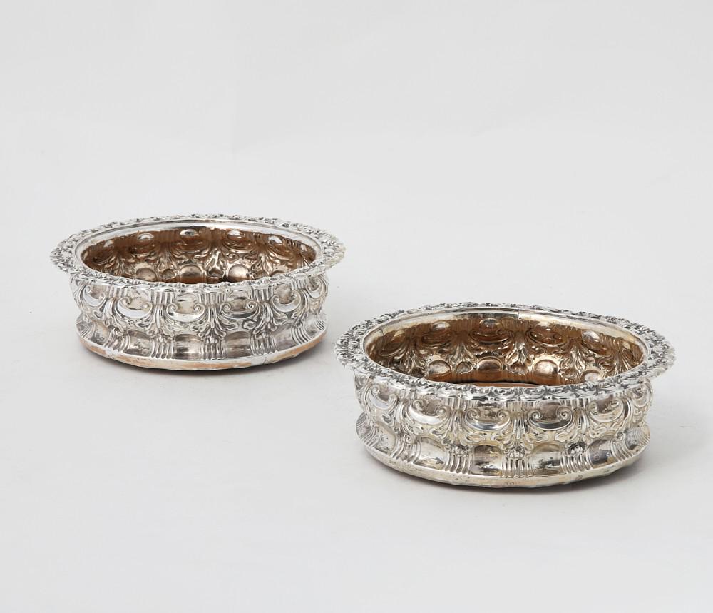 A pair of George IV silver wine bottle coasters: A pair of George IV sterling silver wine bottle coastersJames Kirkby, Gregory & Co., Sheffield1824Central boss engraved with a heraldic crest.height 2in (5cm); diameter 6 1/2in (16.5cm) Provenance: